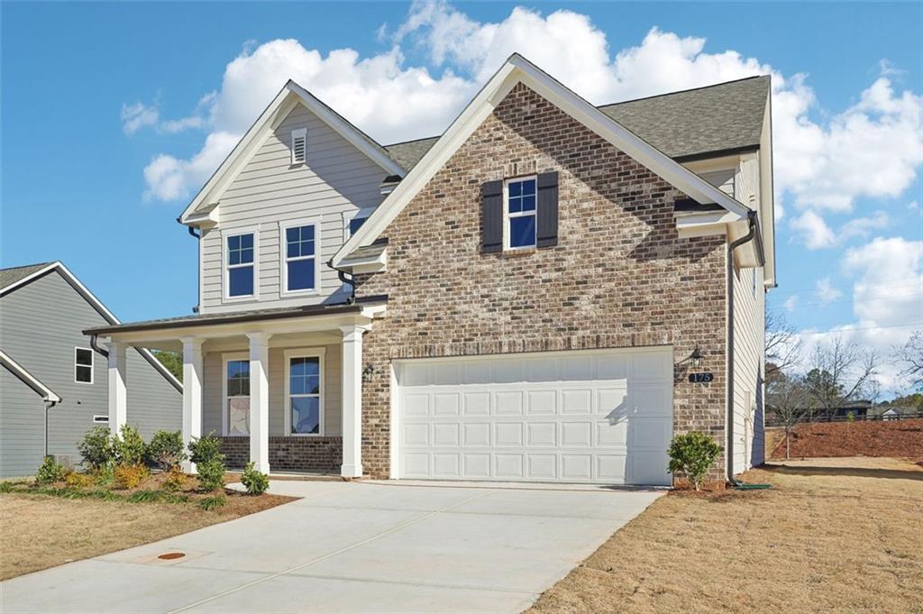 Two-story brick and siding home with covered front porch, two-car garage, and driveway in Wehunt Meadows, Hoschton, Georgia