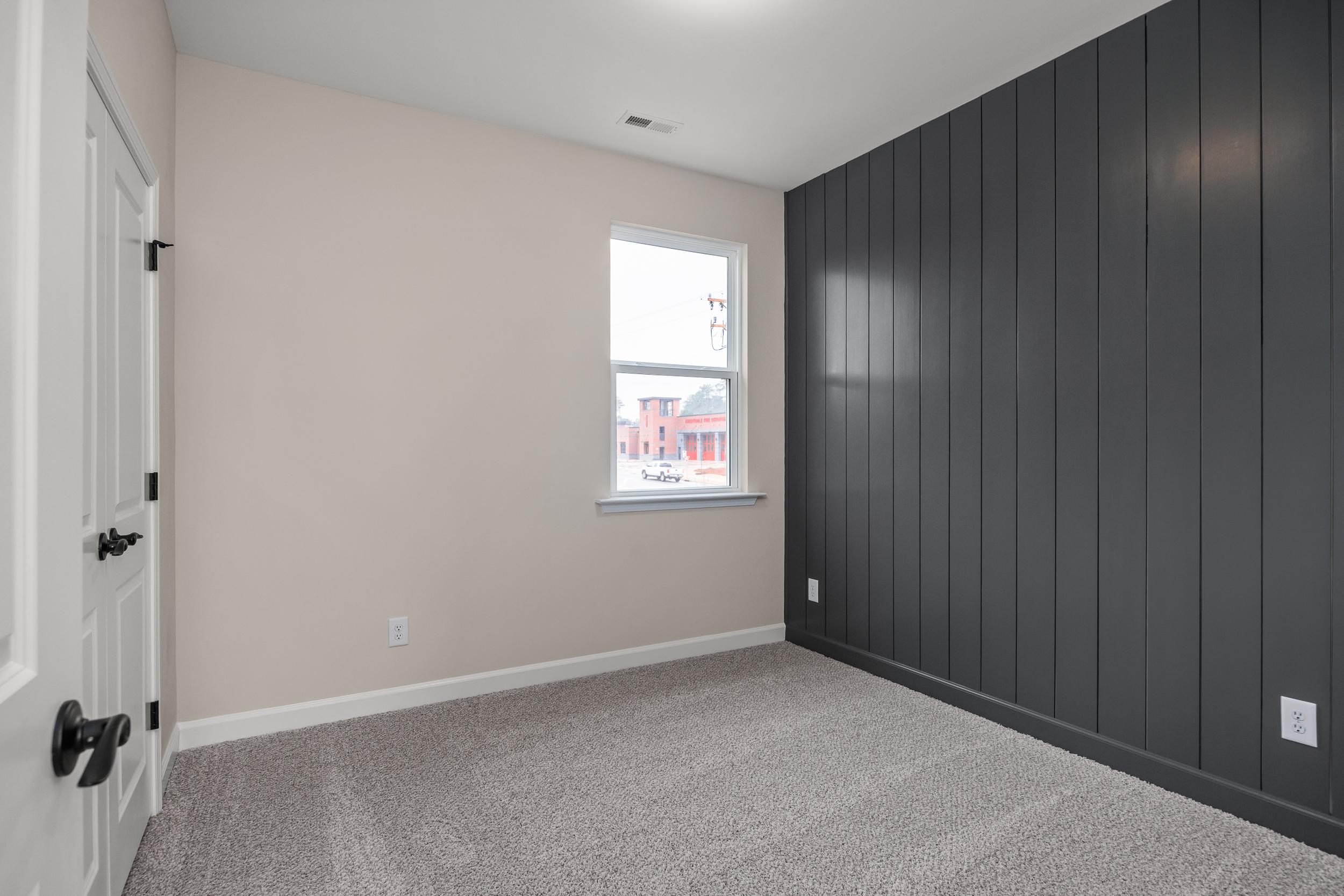 Modern bedroom interior at Forestville Yard in Knightdale NC with dark gray shiplap accent wall, beige trim and carpeted floor