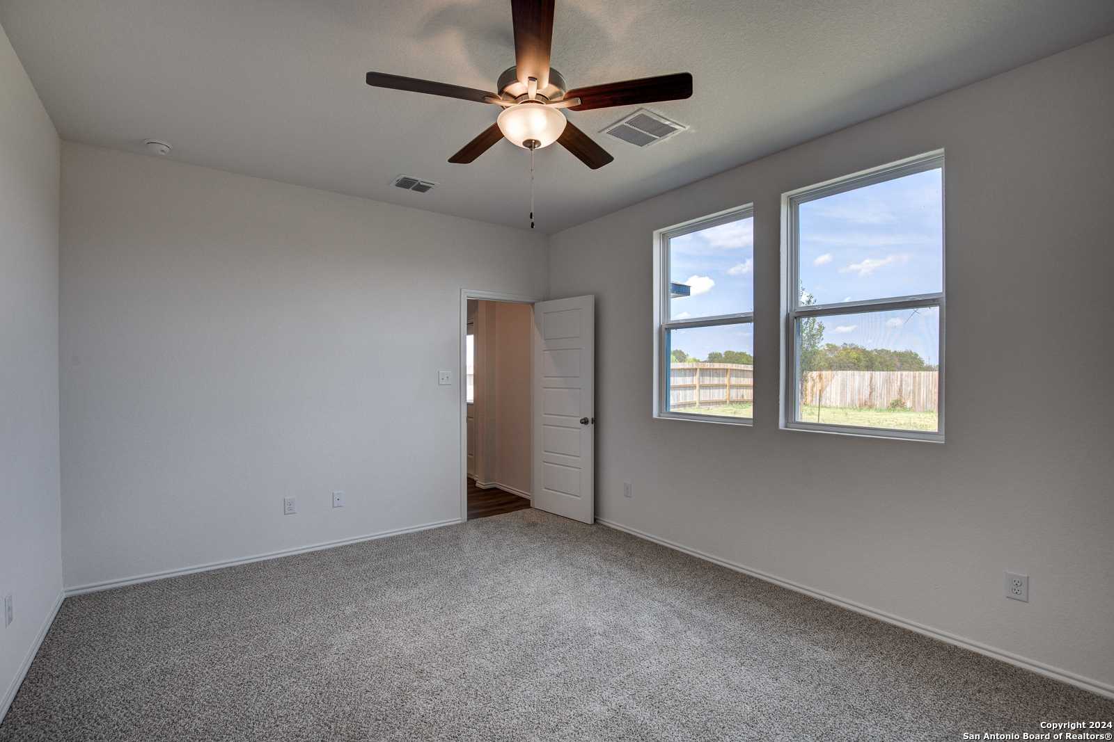 Spacious bedroom with ceiling fan, large windows and beige walls in Davidson Homes The Douglas D, Seguin, Texas