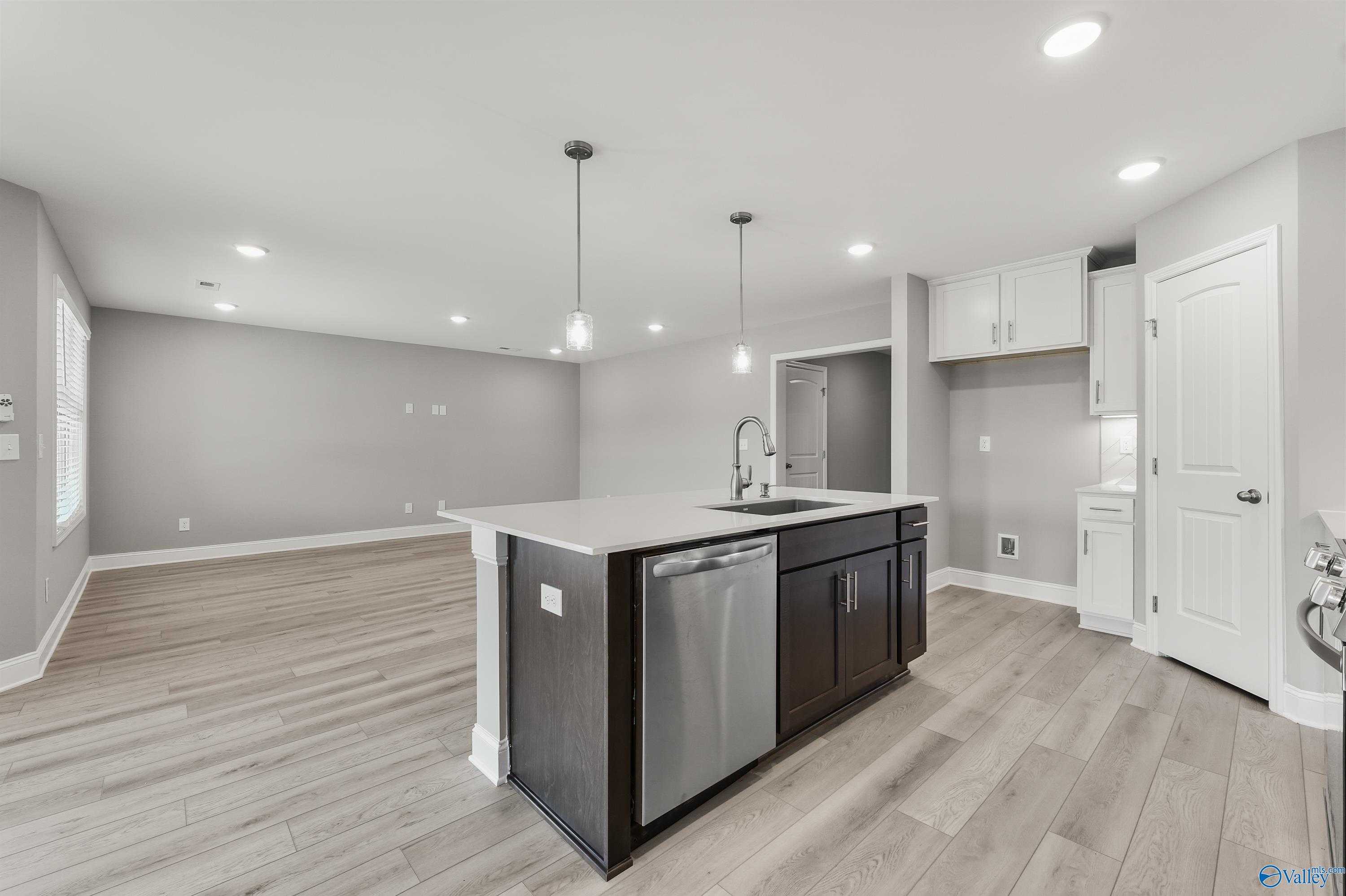 Modern open-concept kitchen with dark island, stainless dishwasher, pendant lights, and hardwood floors in Davidson Homes Everett B, Athens AL
