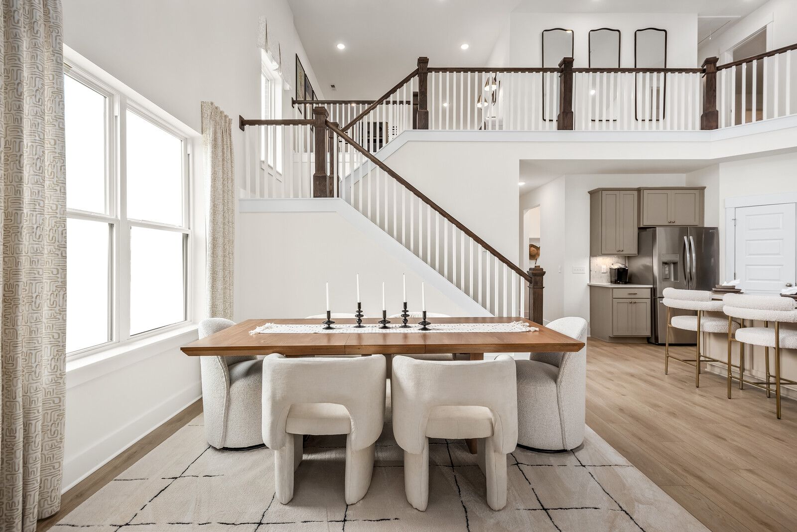 Open-concept dining area in The Ridgeport E by Davidson Homes, Mt. Juliet TN, featuring wooden table, upholstered chairs, kitchen island, and grand staircase