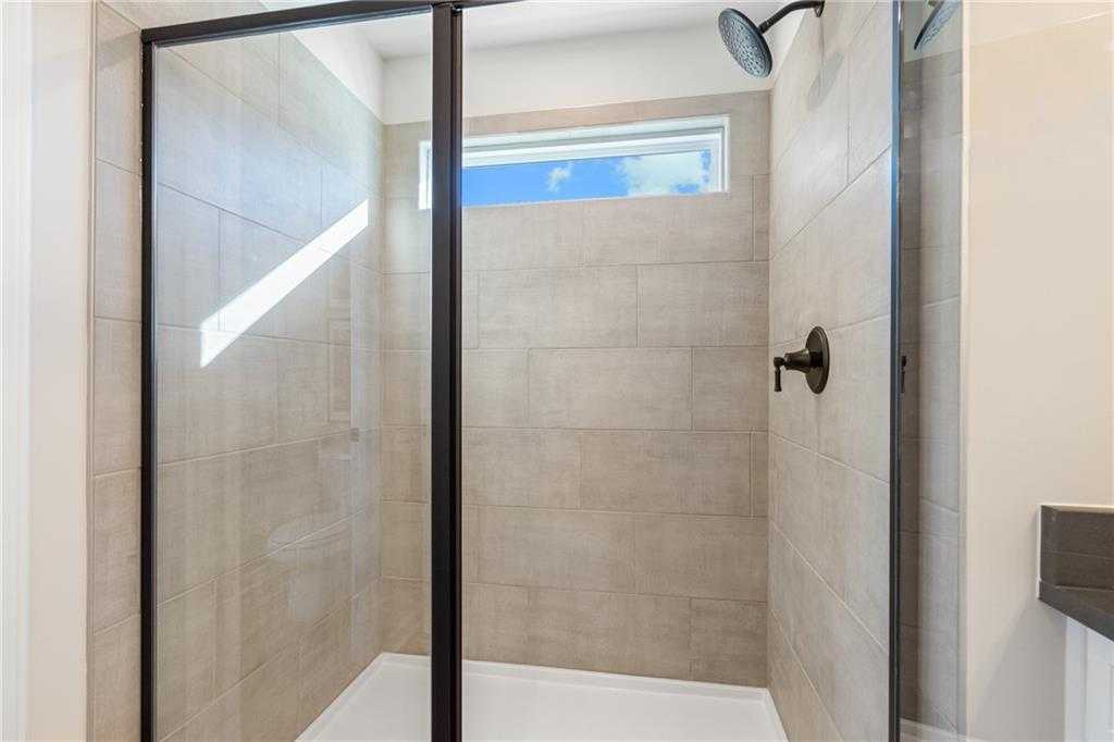 Modern frameless glass shower with rainfall head, beige tiles, and clerestory window in Davidson Homes The Marion C master bath, Winder, Georgia