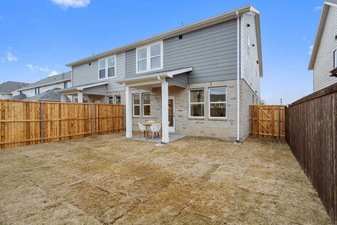 Two-story gray-sided home with covered patio, bistro table, and fenced grassy backyard in Lake Park Villas, Wylie, Texas