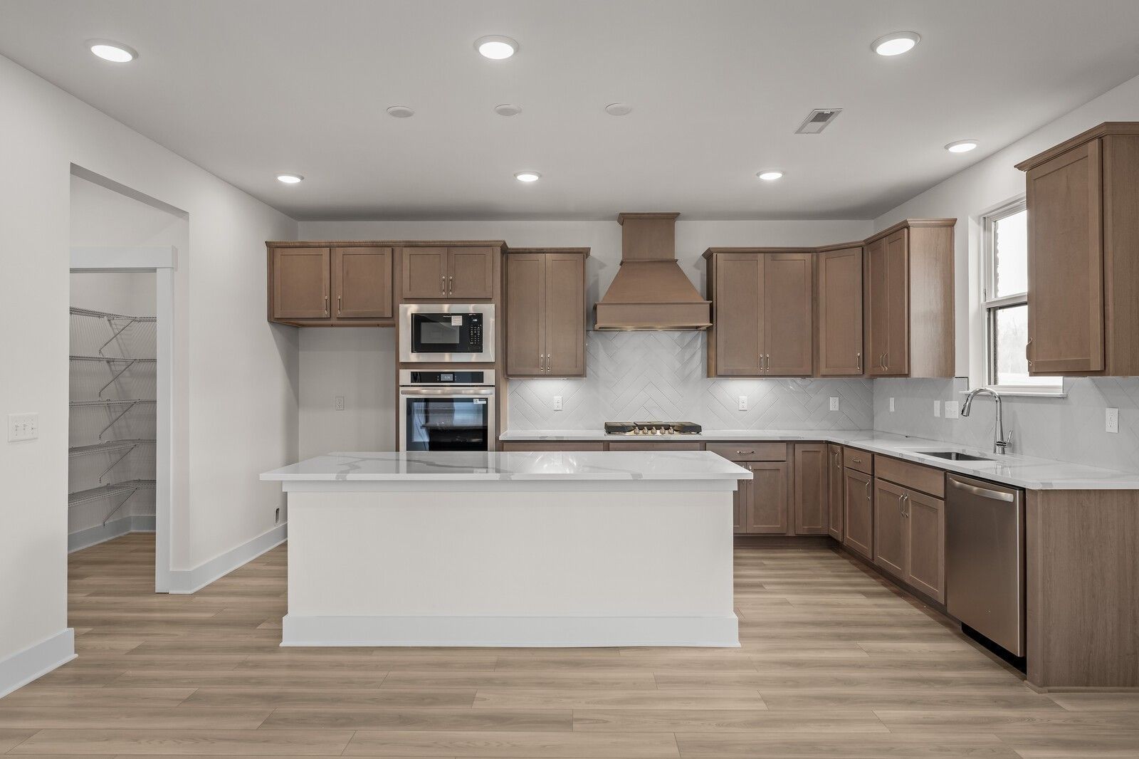 Modern kitchen with white island, wood cabinetry, and walk-in pantry in The Henry C floor plan, Benders Cove, Mt. Juliet.