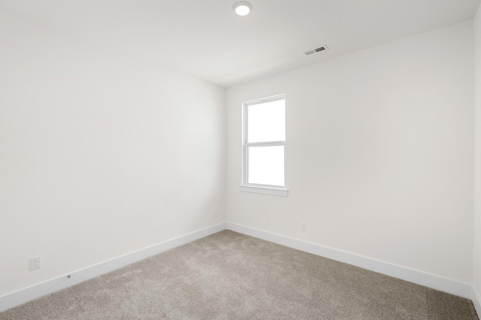 Bright bedroom with neutral walls and carpet in The Cottonwood E floor plan at Woods Crossing in Gallatin, Tennessee.