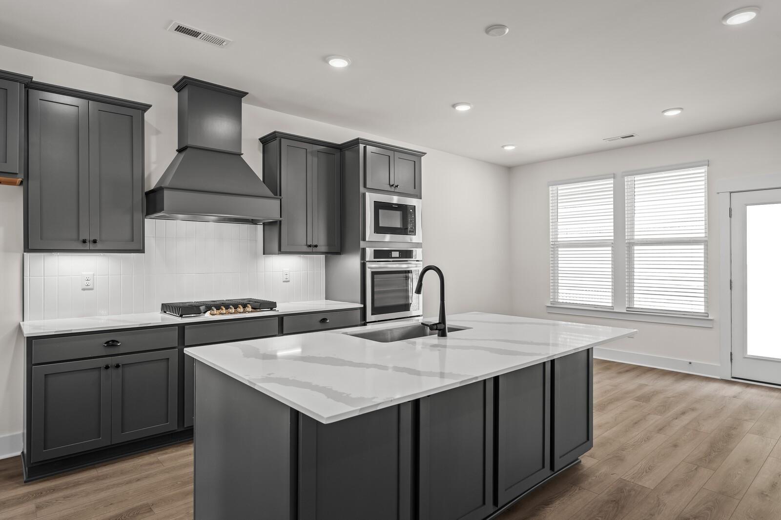 Modern kitchen with dark gray cabinets, quartz island, and stainless appliances in The Willow floor plan, Gallatin, TN.