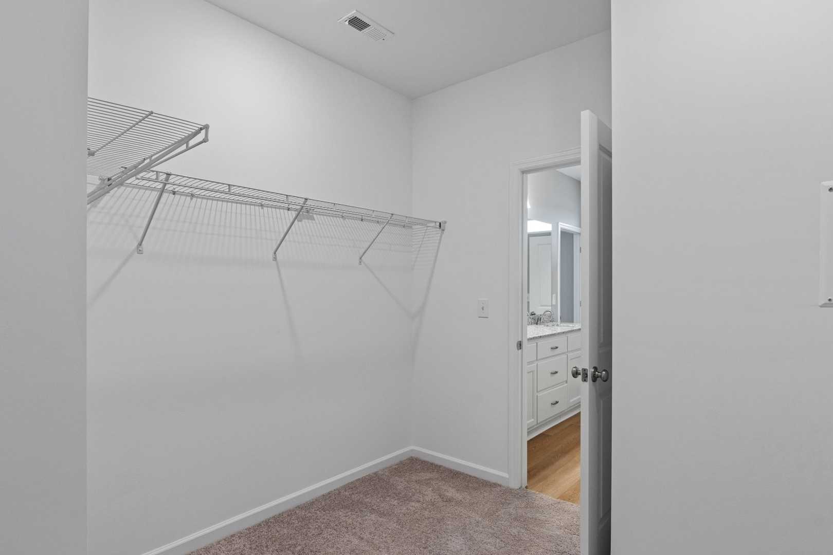 Spacious walk-in closet in The Stella master suite with wire shelving, hanging rods, and adjacent bathroom vanity