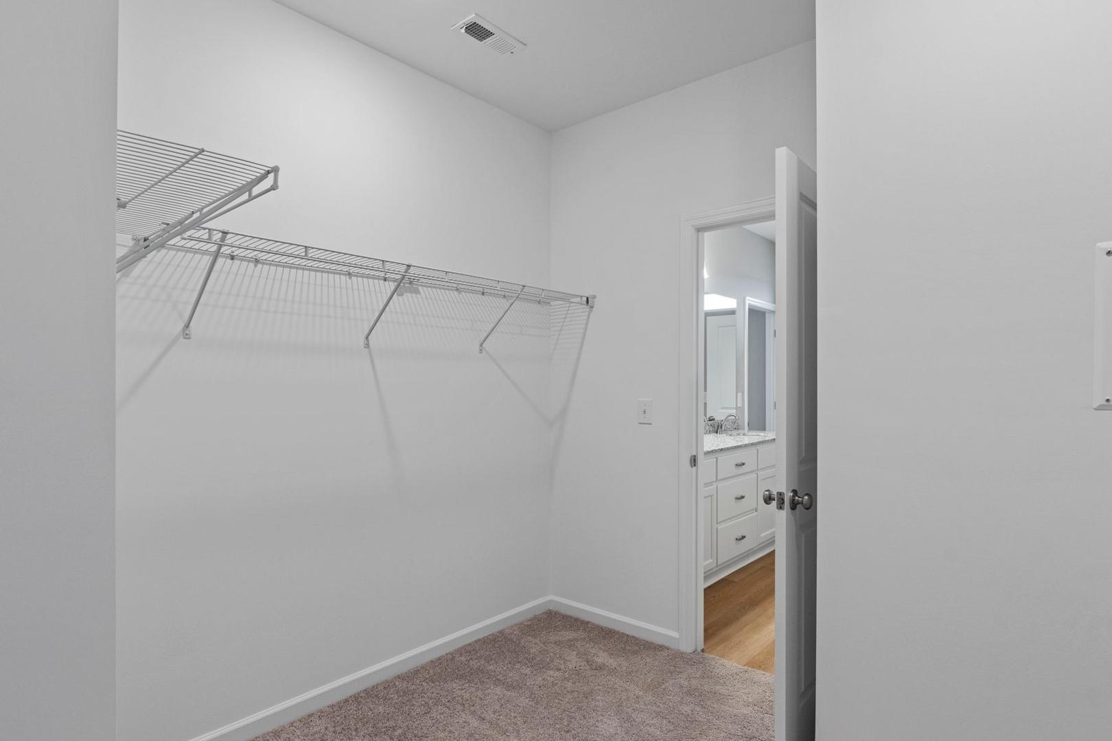 Spacious walk-in closet in The Stella A master suite featuring wire shelving, hanging rods, and adjacent en-suite bathroom