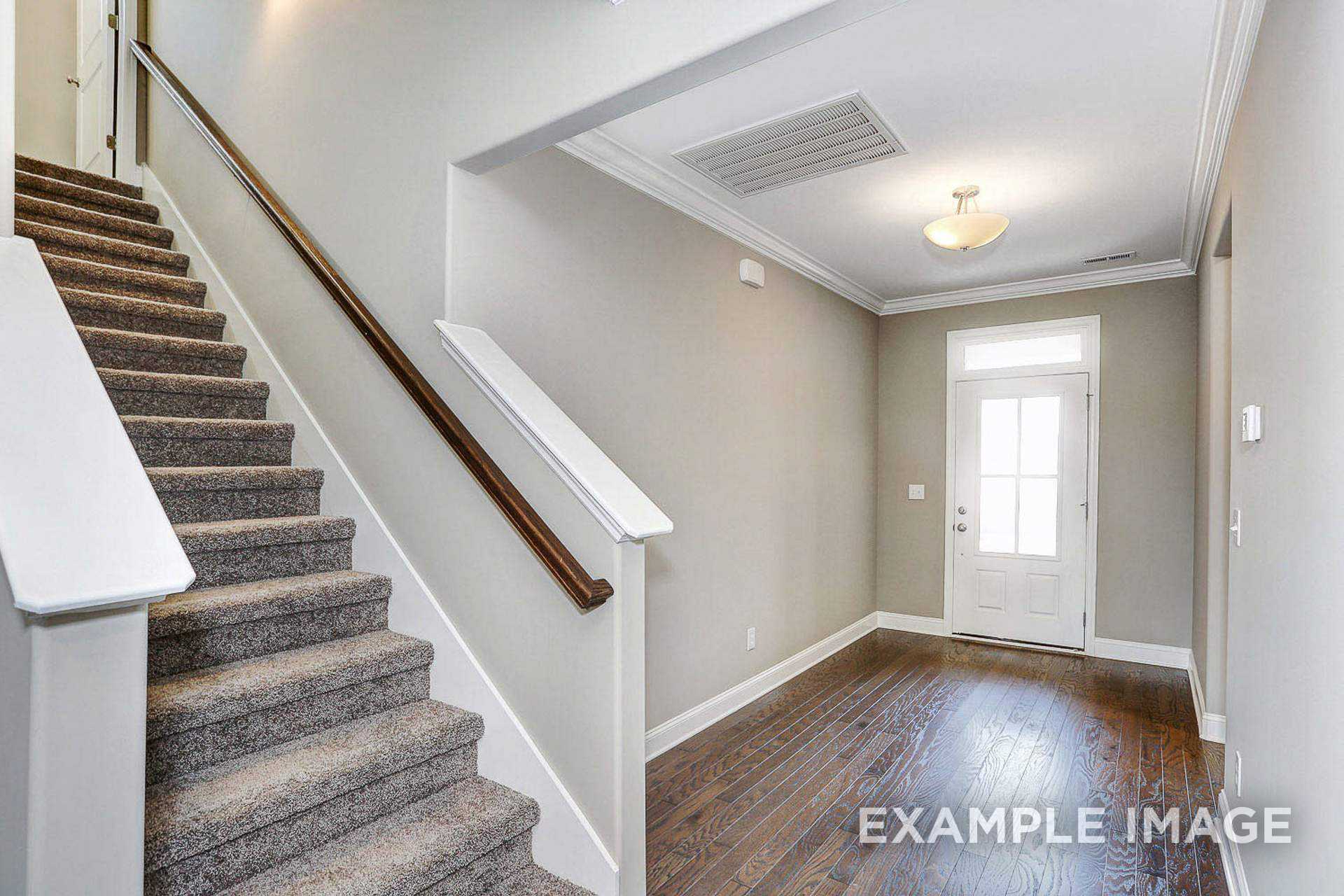 Grand staircase and entry foyer in The Montgomery B 2-story home with light gray walls, carpeted steps, wood handrails, and hardwood floors