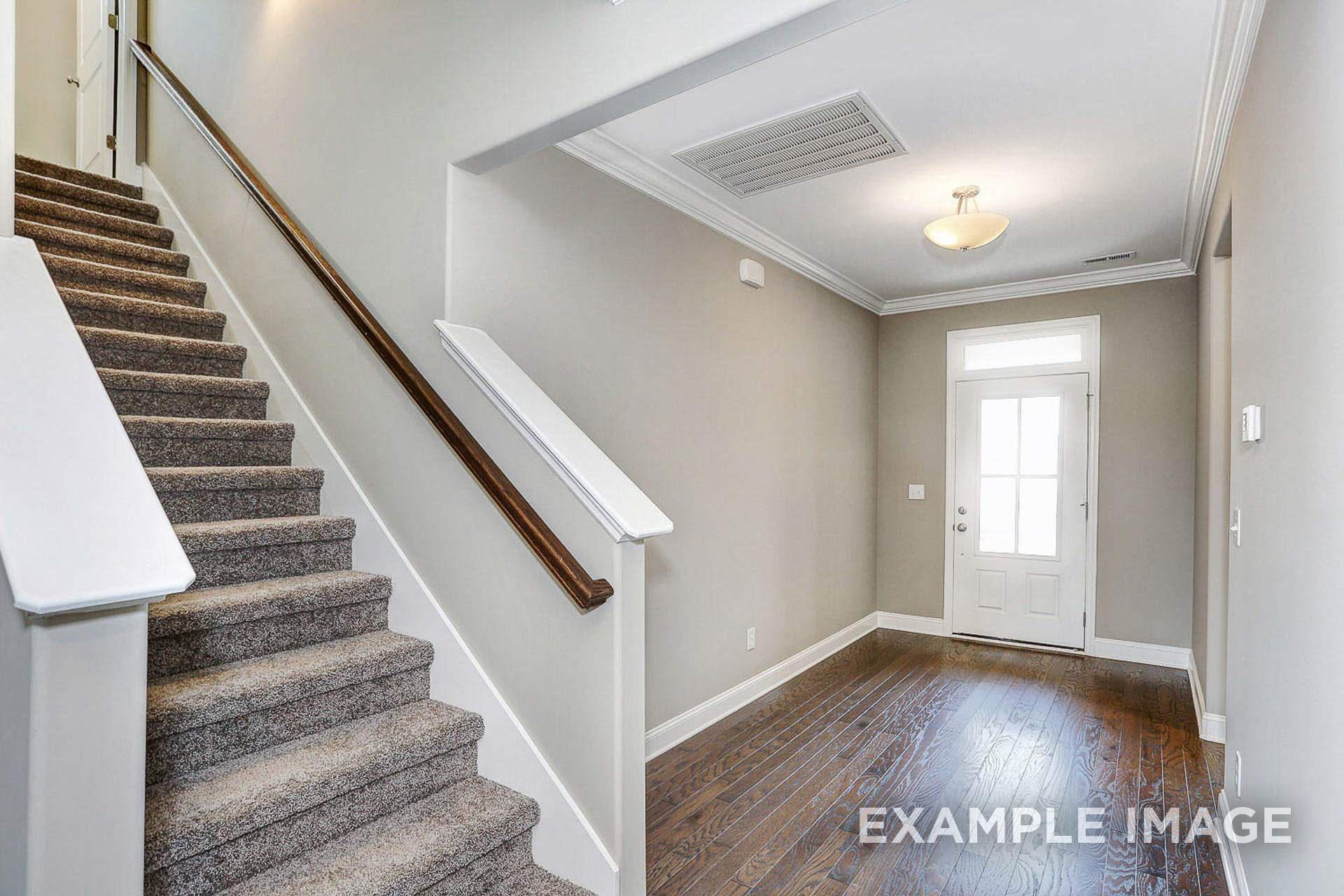 Spacious foyer with carpeted staircase, wood handrails, and hardwood floors in The Montgomery C 2-story home