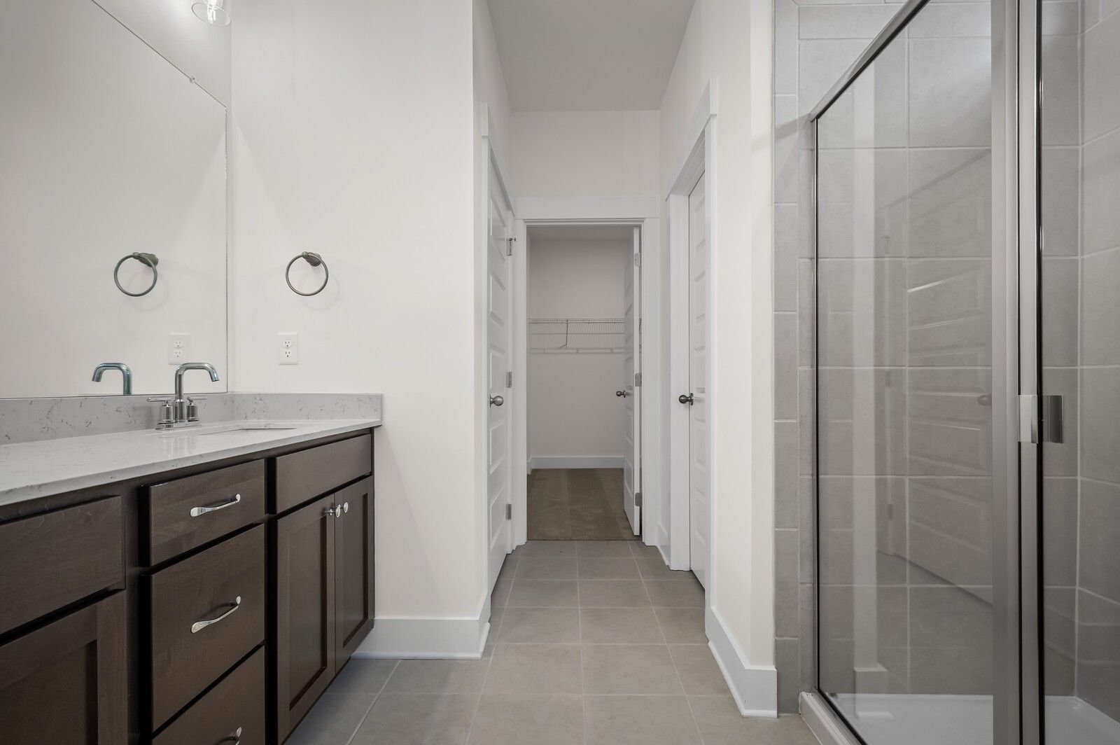 Modern bathroom with dark wood vanity, quartz countertop, and glass-enclosed shower in The Ash A home at Woods Crossing.