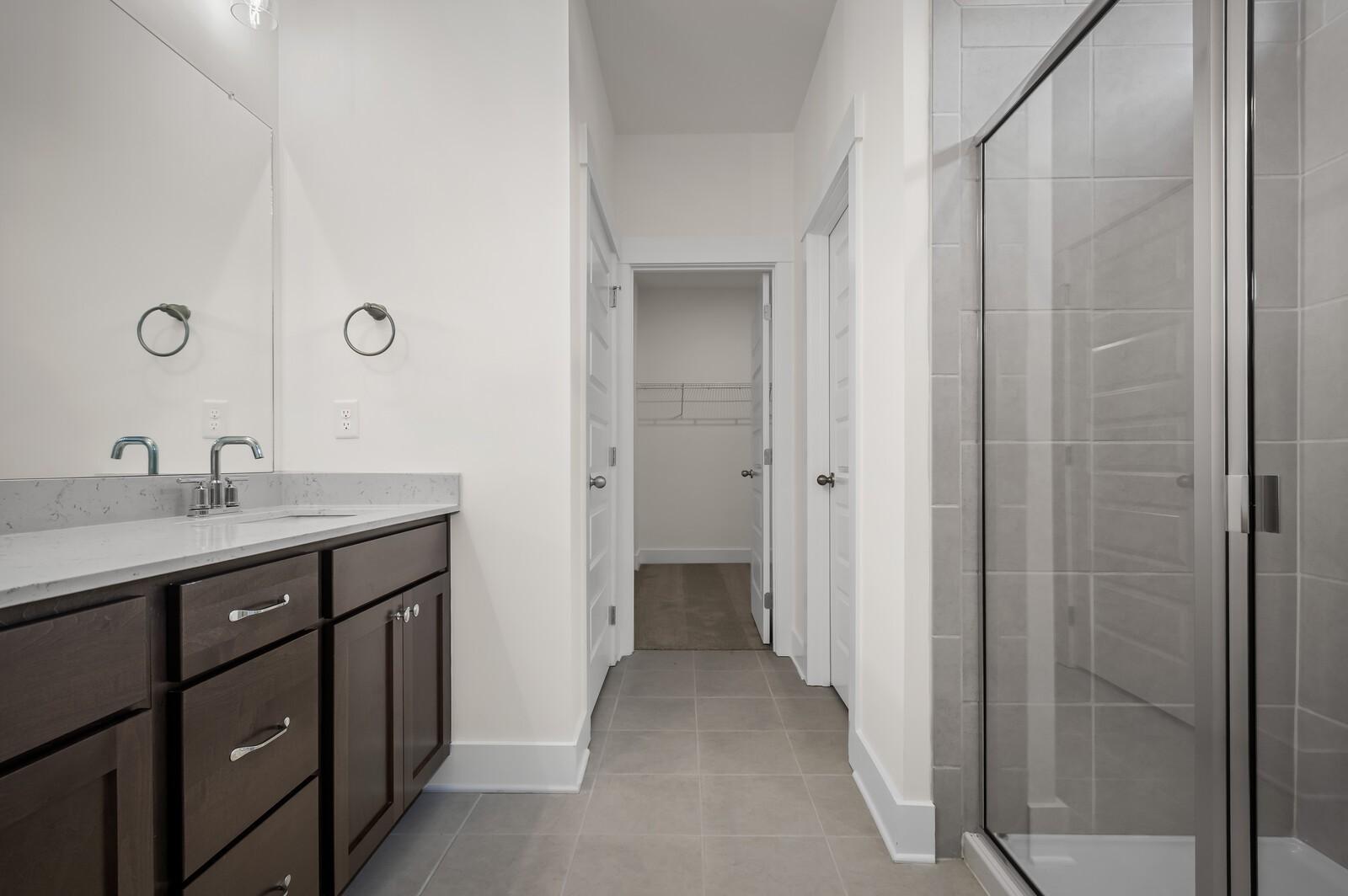 Modern bathroom with dark wood vanity, quartz countertop, and glass-enclosed shower in The Ash A home at Woods Crossing.