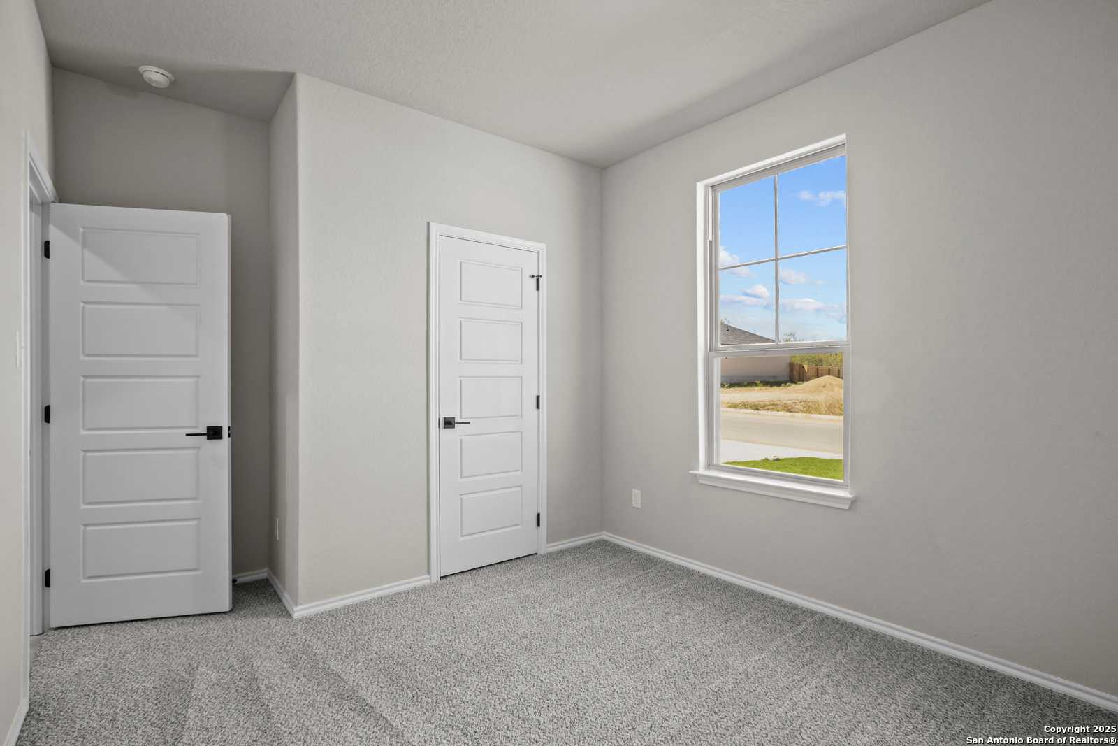 Bright bedroom with neutral walls, white doors, carpet floor, and large window in The Asheville E by Davidson Homes, Converse, Texas