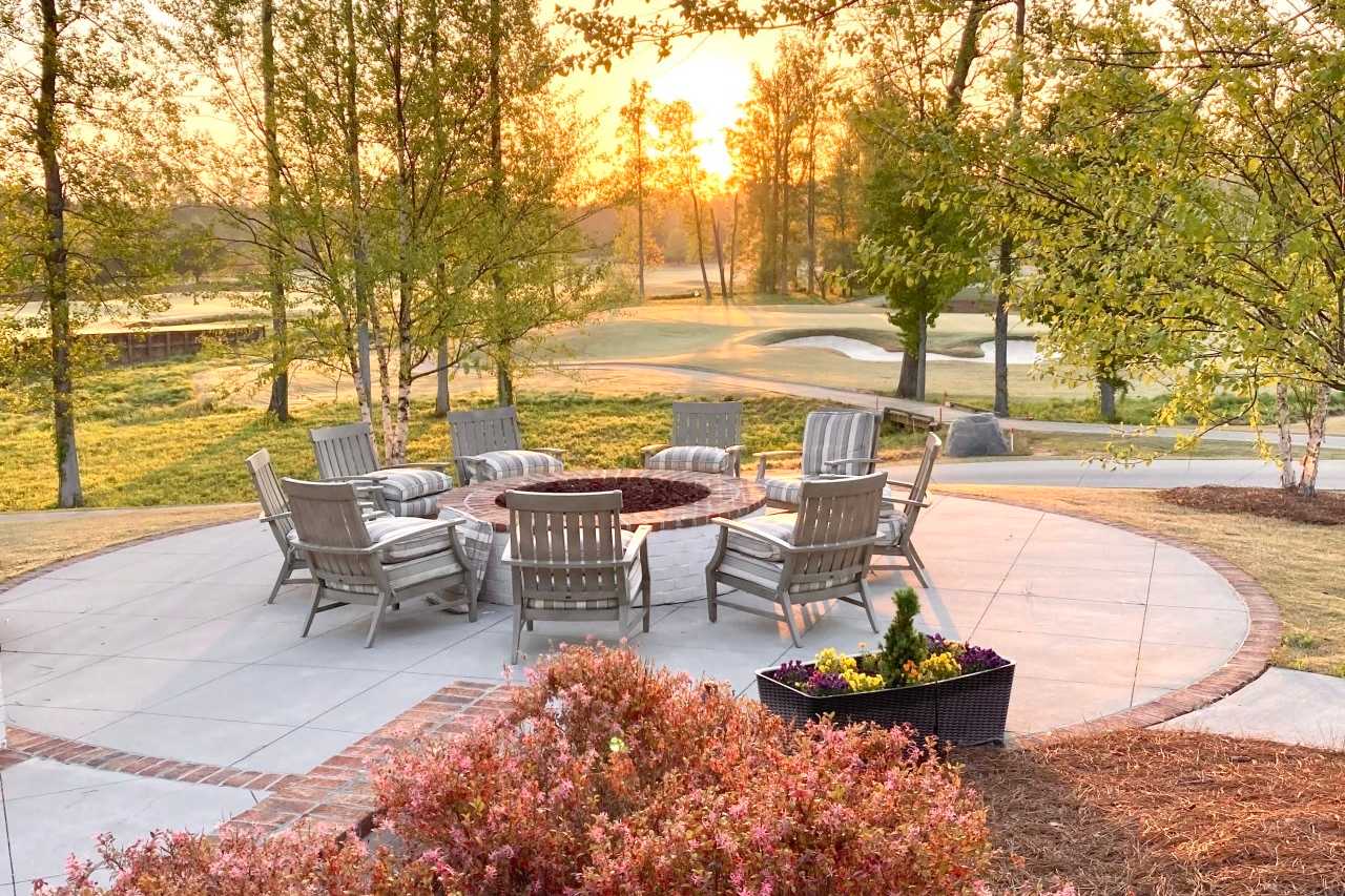 Cozy circular fire pit patio at Addison West in Holly Springs NC with Adirondack chairs, potted flowers and sunset trees