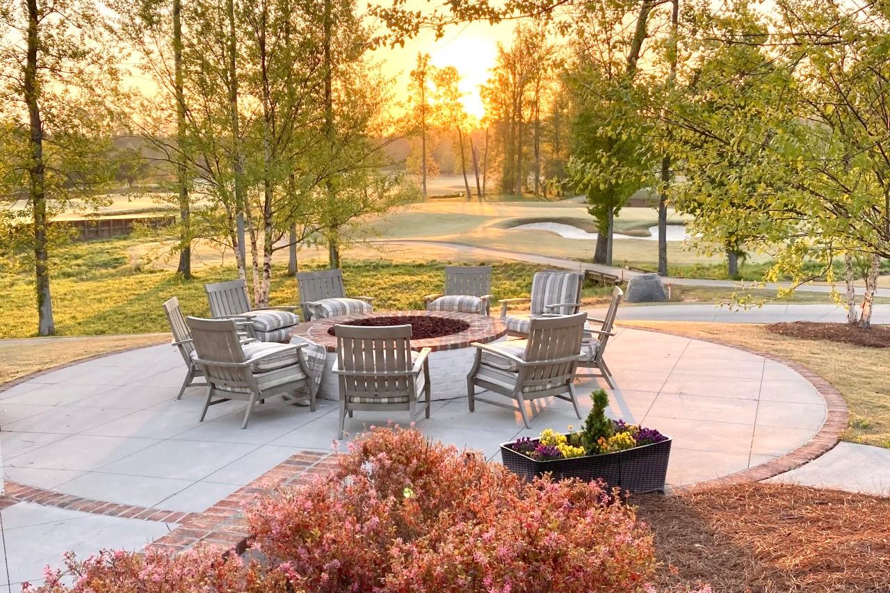 Cozy circular fire pit patio at Addison West in Holly Springs NC with Adirondack chairs, potted flowers and sunset trees