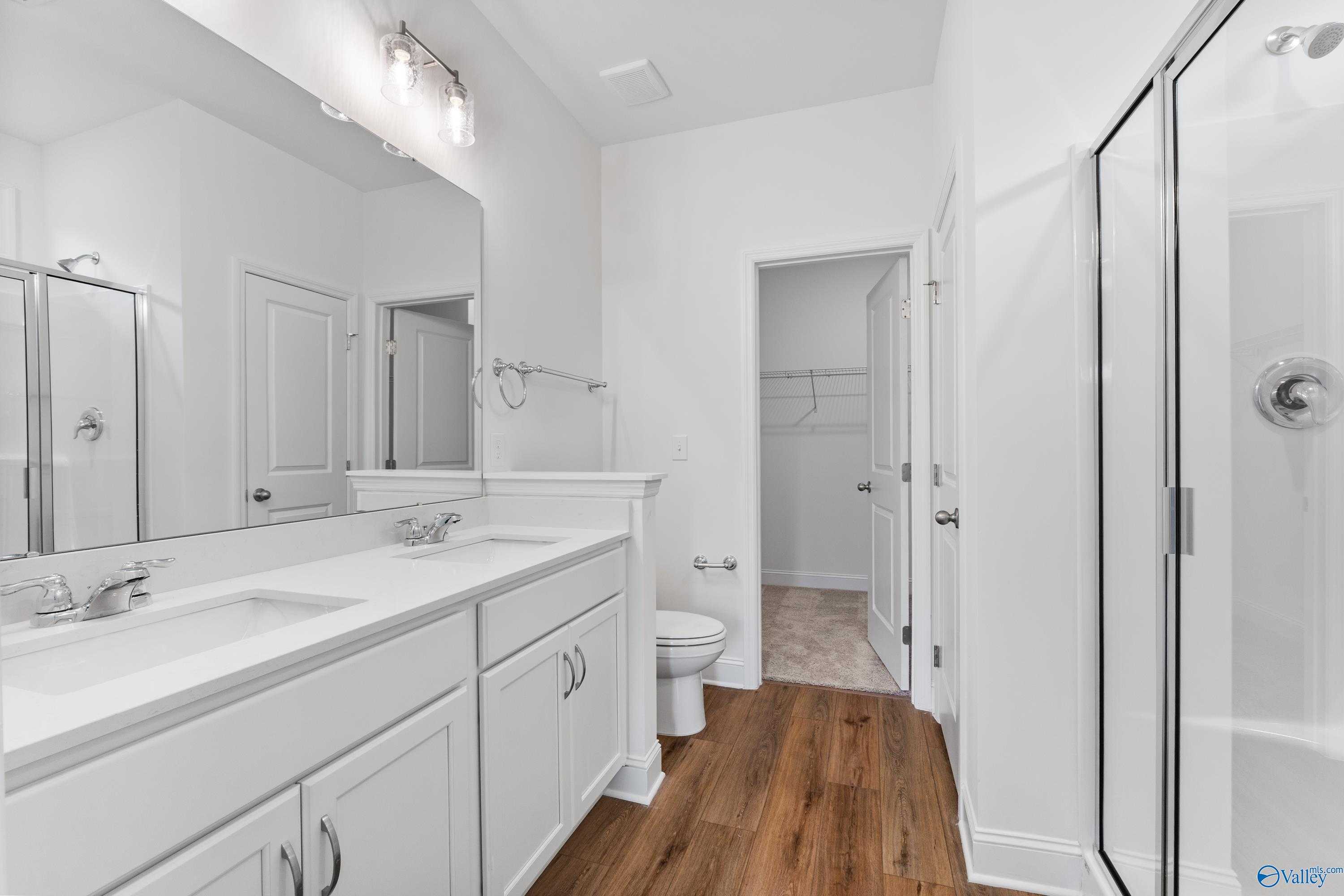Modern master bathroom with double vanity, frameless glass shower, and adjacent walk-in closet in Davidson Homes The Asheville C, New Market, Alabama