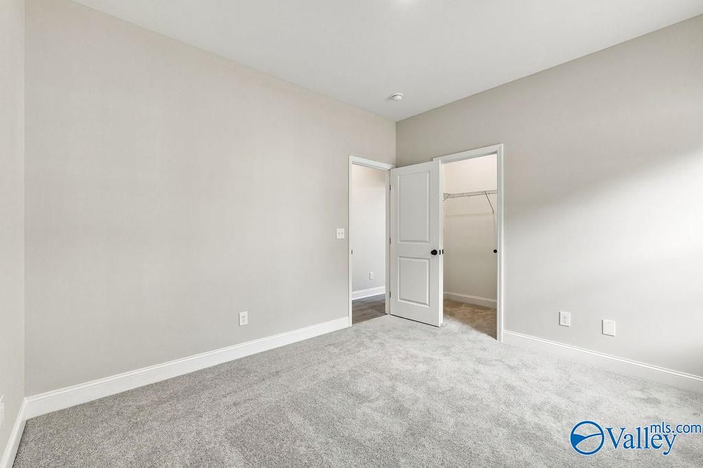 Spacious carpeted bedroom with neutral walls, walk-in closet, and white trim in Davidson Homes Rockford plan, Hartselle, Alabama