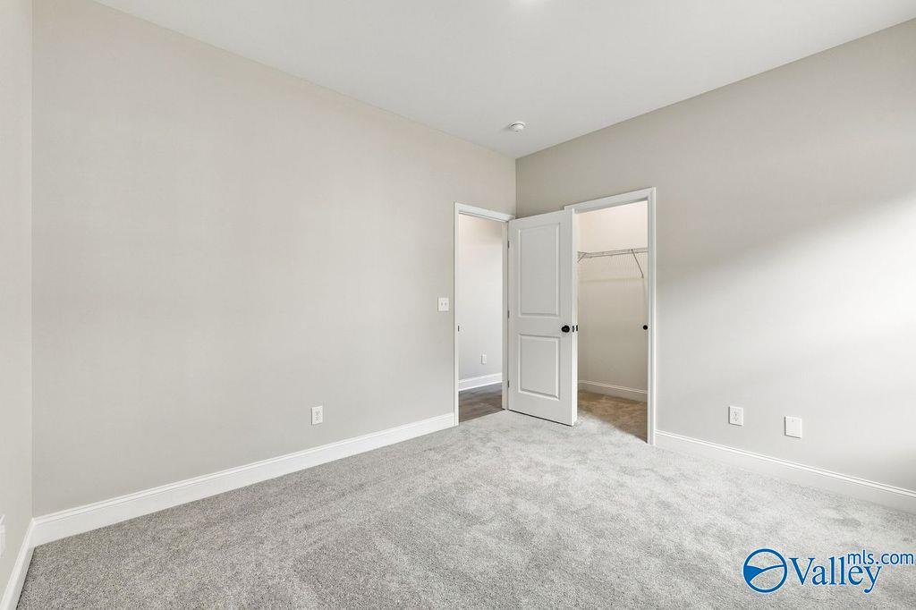 Spacious carpeted bedroom with neutral walls, walk-in closet, and white trim in Davidson Homes Rockford plan, Hartselle, Alabama