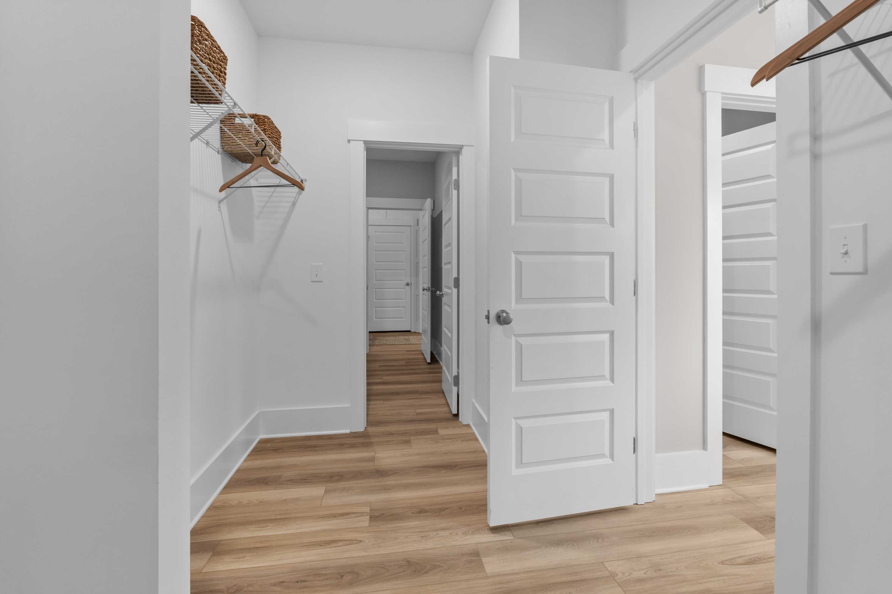 Spacious walk-in closet at The Highlands in Arab Alabama with open white panel doors, wooden hangers, woven baskets, and light oak floors