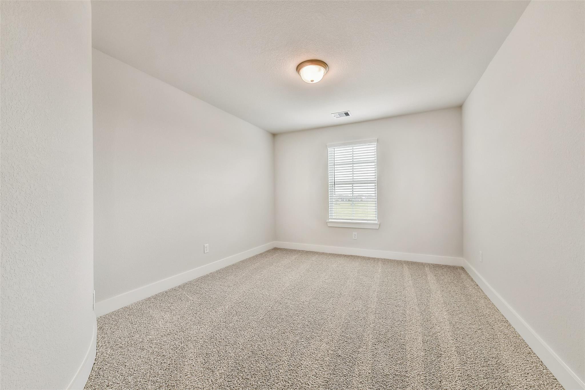 Empty secondary bedroom featuring white walls, neutral carpet, window blinds, and ceiling light in Davidson Homes The Victoria A, Lago Mar, Texas City