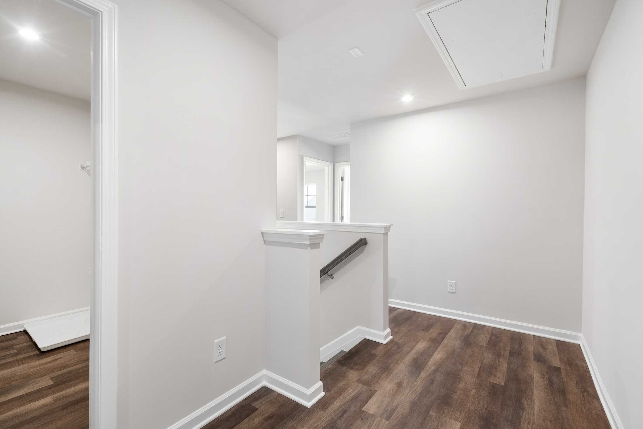 Spacious interior hallway in The Cary B two-story home featuring white staircase railing and oak hardwood floors