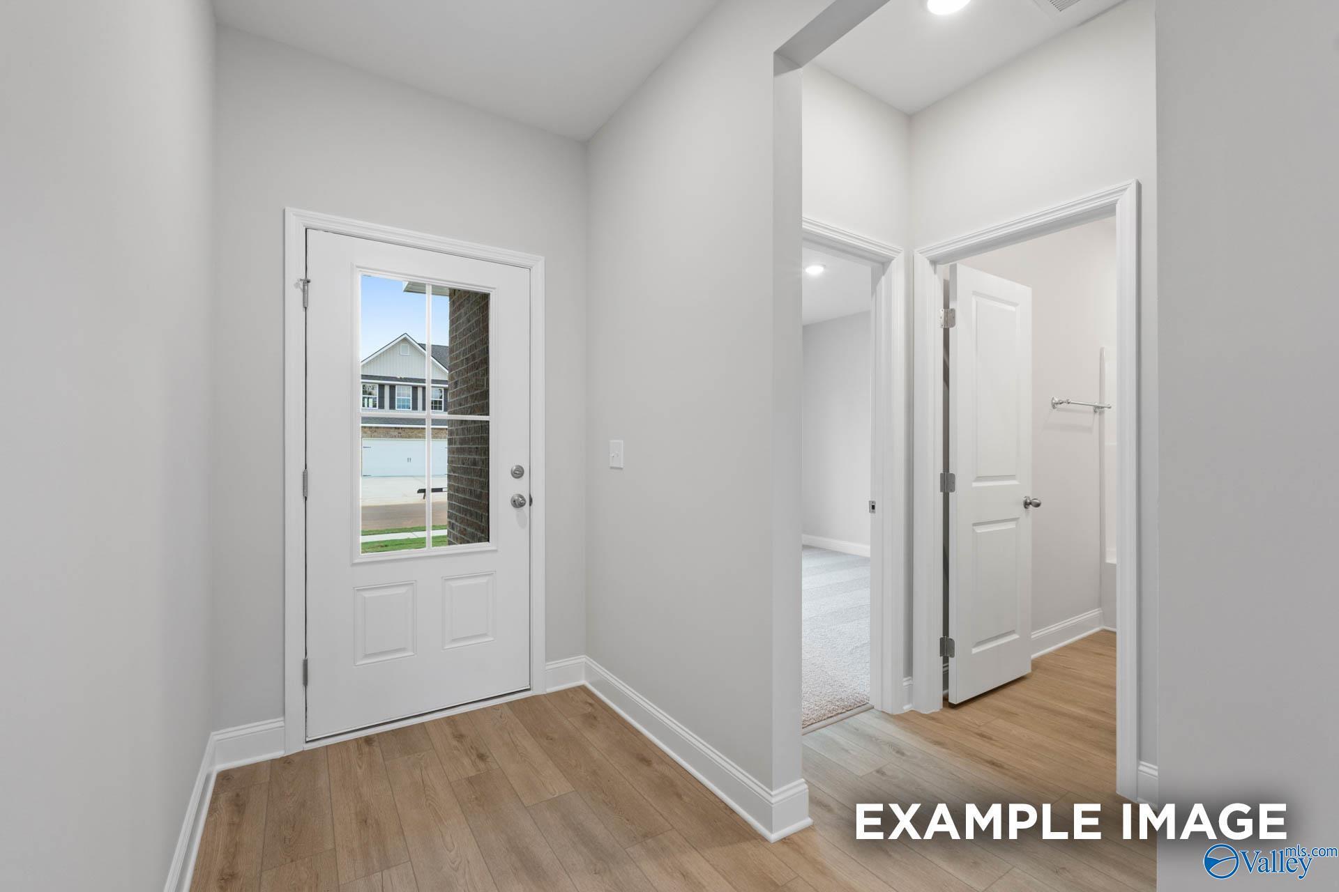 Bright entry foyer with light gray walls, hardwood floors, and glass front door overlooking lawn in Davidson Homes The Franklin C, Toney, Alabama