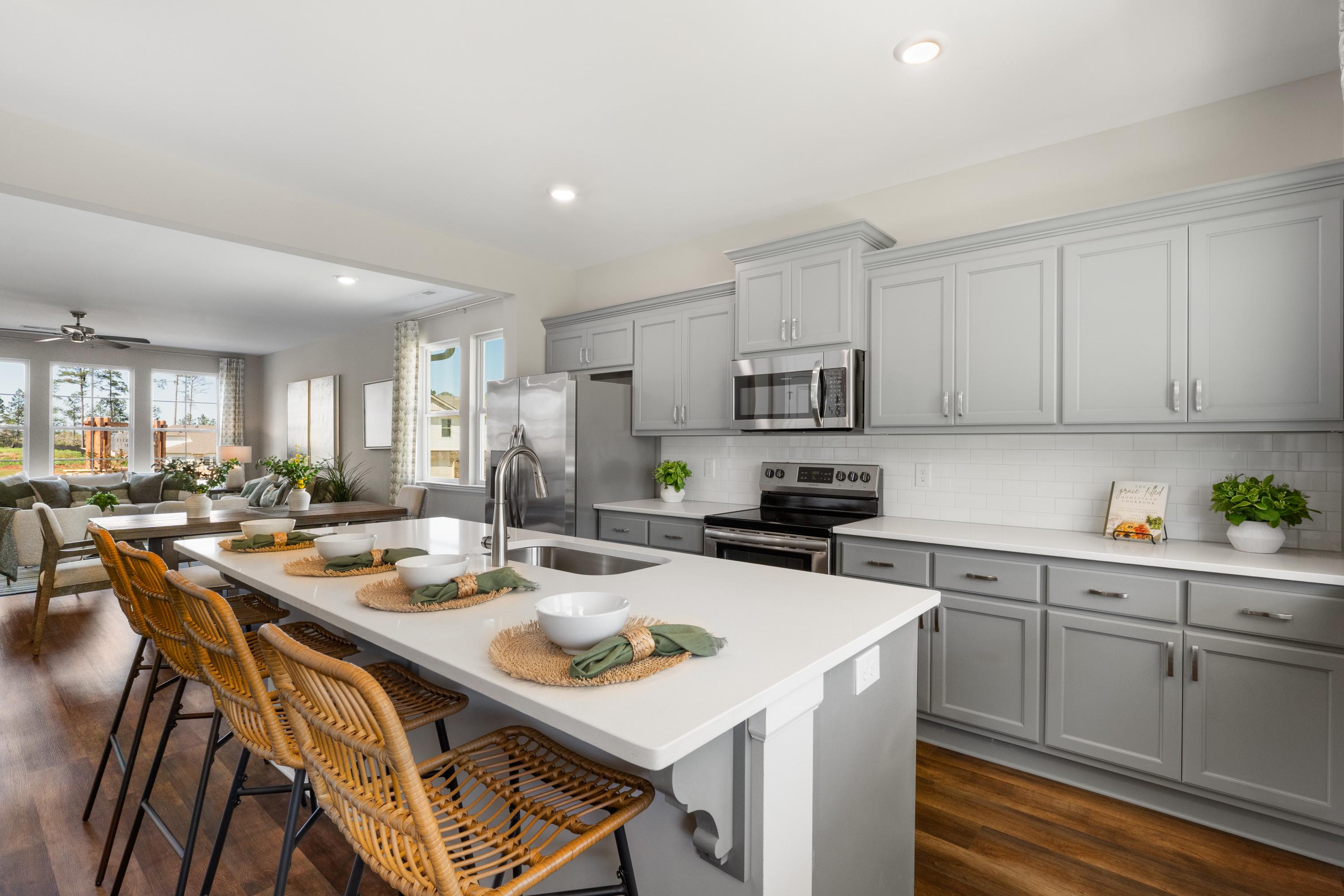 Open-concept kitchen in Evergreen Mill Madison Alabama with gray cabinets stainless steel appliances and rattan island stools