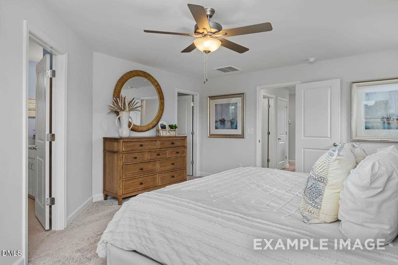 Serene master bedroom with plush white bed, wooden dresser, round mirror, and ceiling fan in Davidson Homes The Graham, Fuquay-Varina, NC