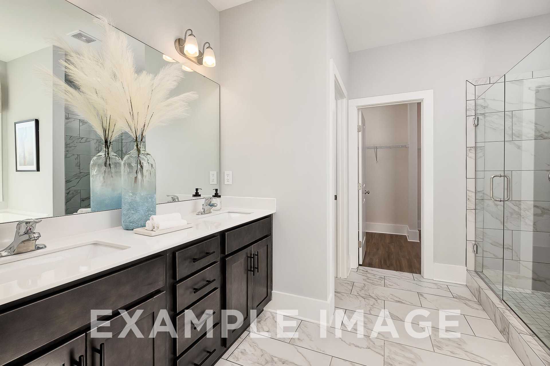 Modern master bathroom in The Everett B featuring double vanity, frameless glass shower, walk-in closet