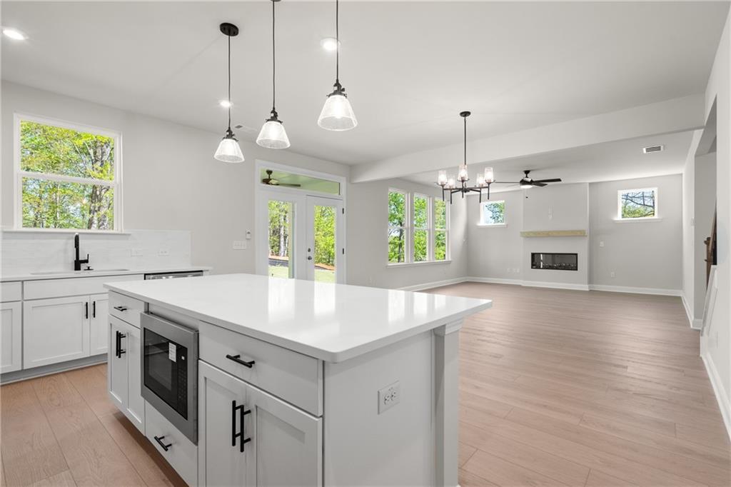 Modern open-concept kitchen with white quartz island, pendant lights, and gas fireplace living area in Davidson Homes The Hickory E, Buford, GA
