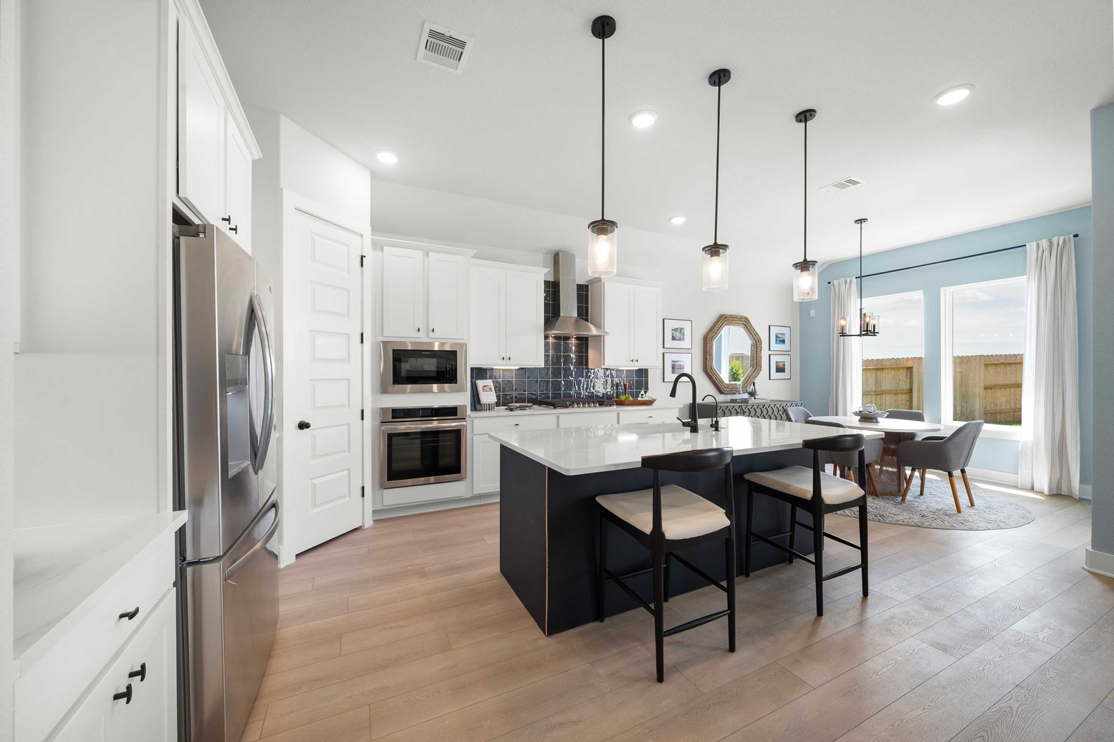 Modern kitchen at Lago Mar in Texas City TX with white cabinets, quartz island, black bar stools, hardwood floors, and pendant lights