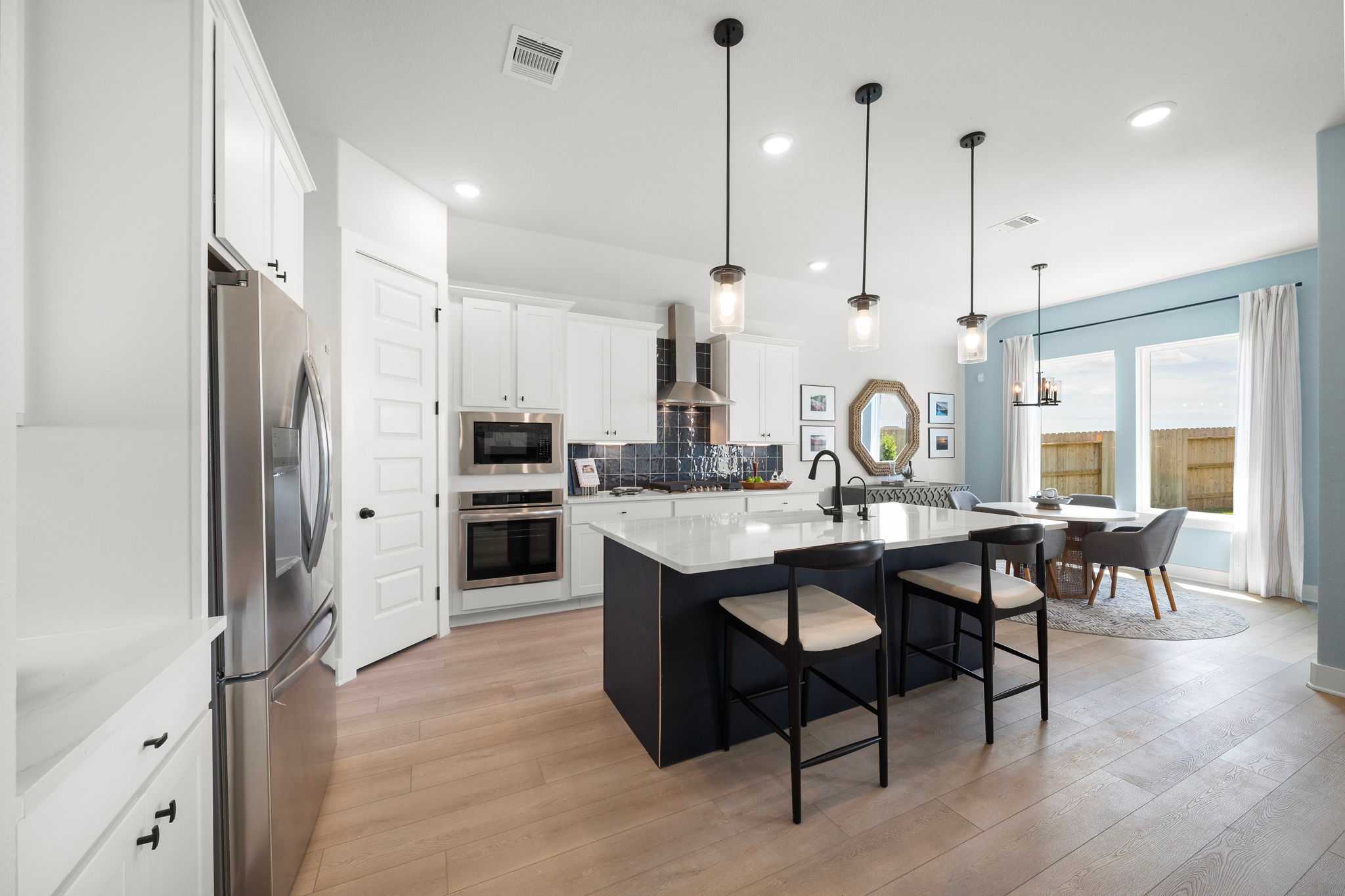 Modern kitchen at Lago Mar in Texas City TX with white cabinets, quartz island, black bar stools, hardwood floors, and pendant lights