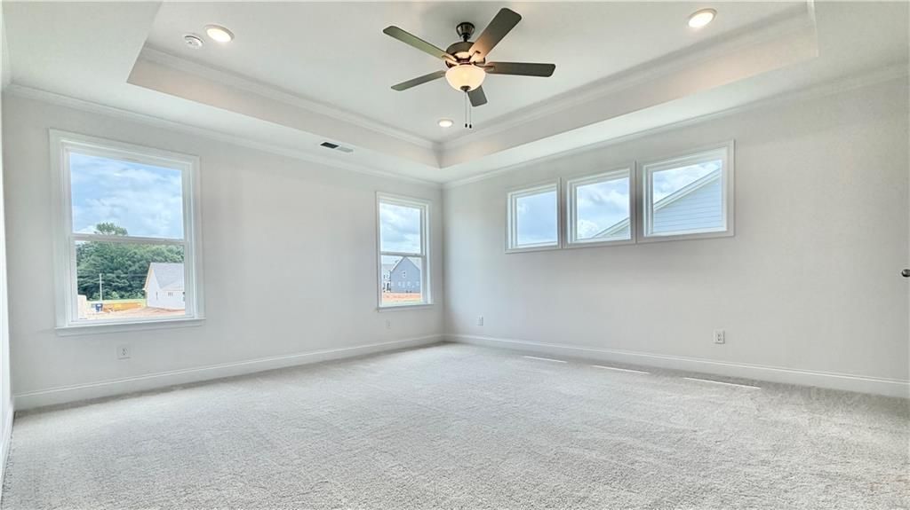Spacious primary bedroom with tray ceiling and ceiling fan in The Hickory C floor plan at Wehunt Meadows, Hoschton, GA.