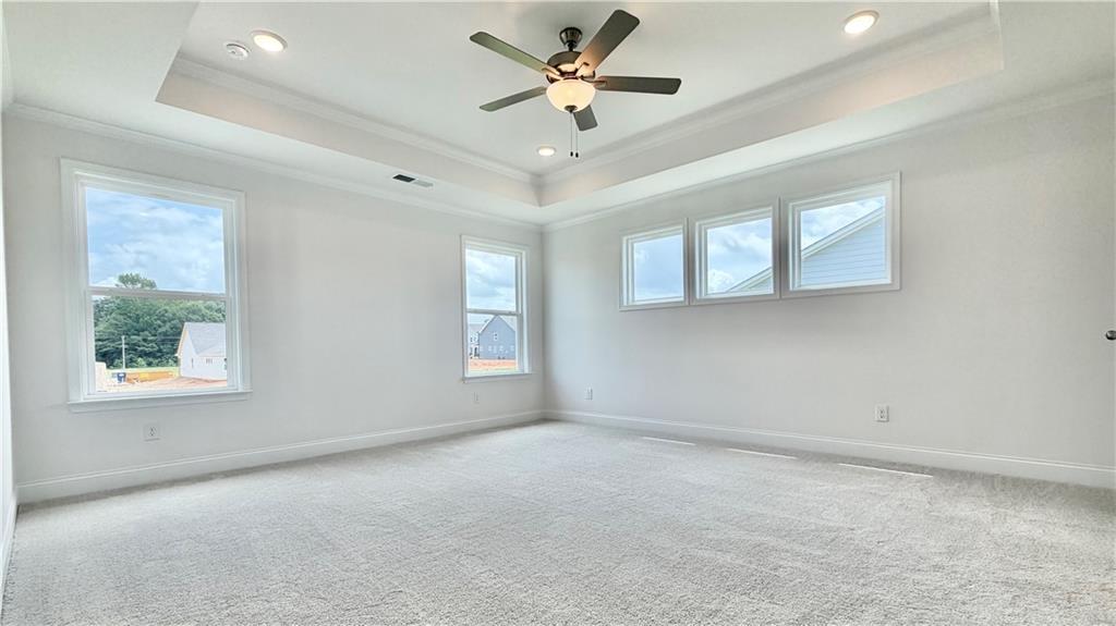 Spacious primary bedroom with tray ceiling and ceiling fan in The Hickory C floor plan at Wehunt Meadows, Hoschton, GA.