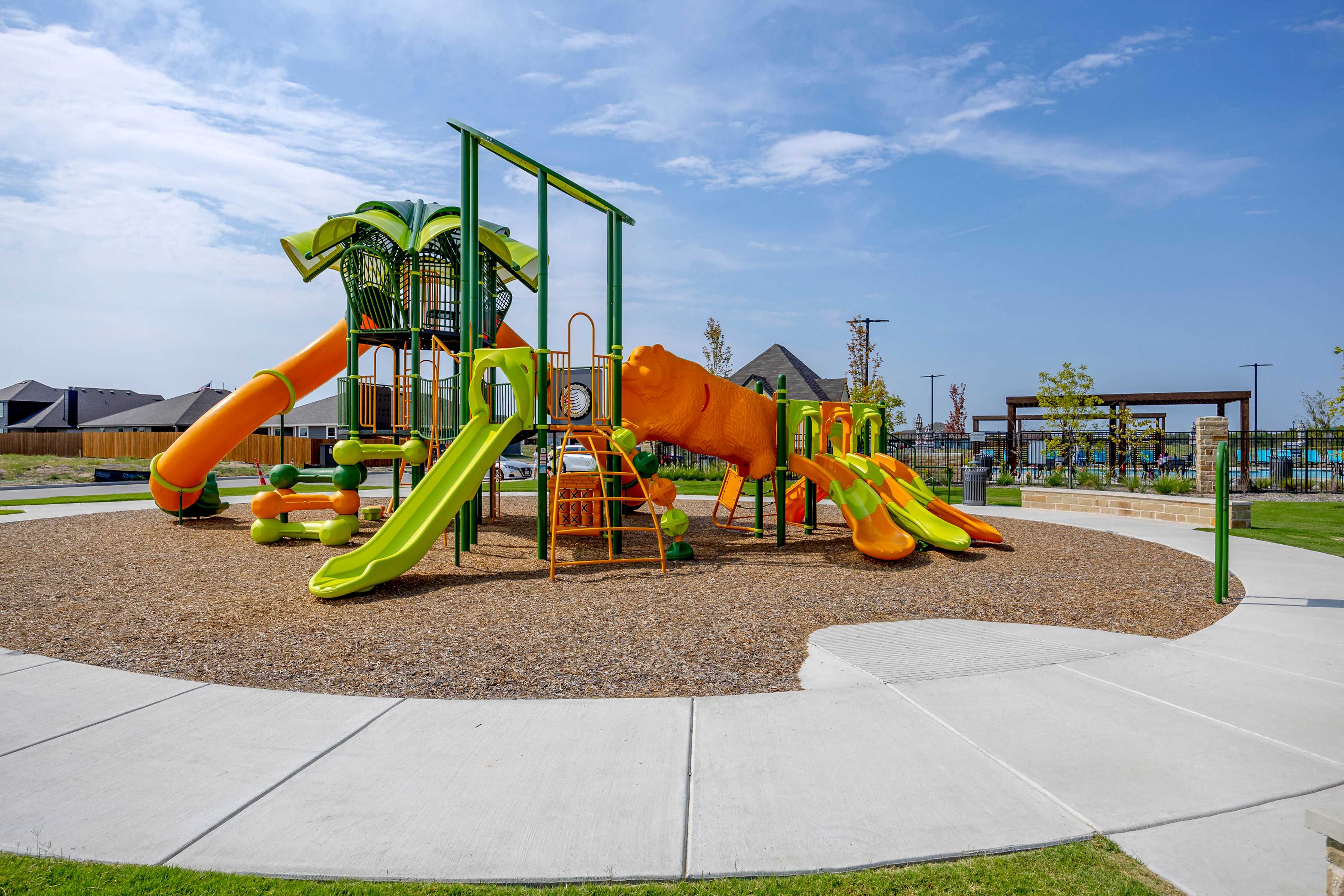 Vibrant playground with orange slides, green climbing structures and palm tree elements at Waverly Estates in Josephine, Texas