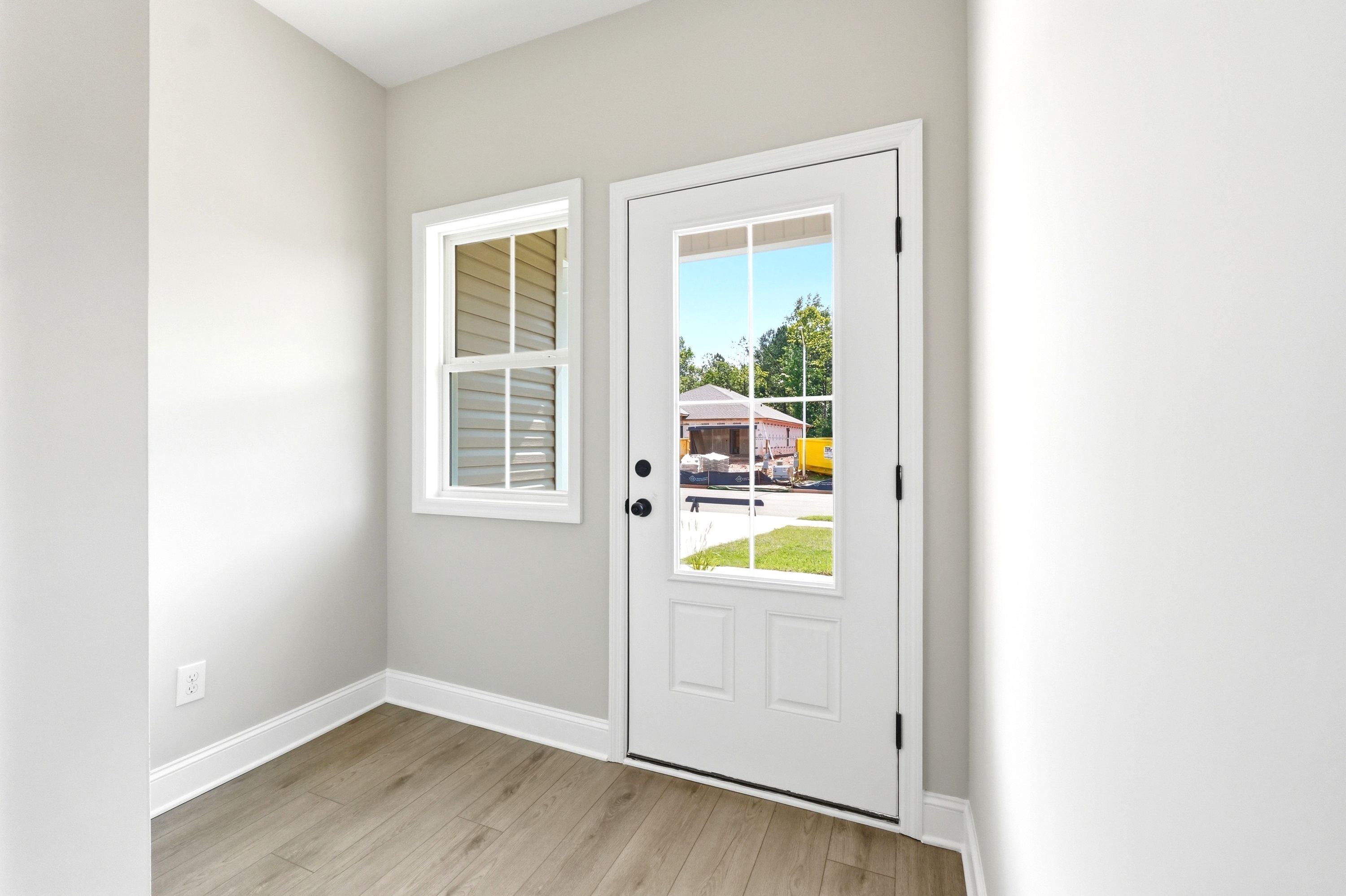 Bright entryway of The Russell A featuring modern light wood flooring, neutral walls, and a glass-paneled exterior door.