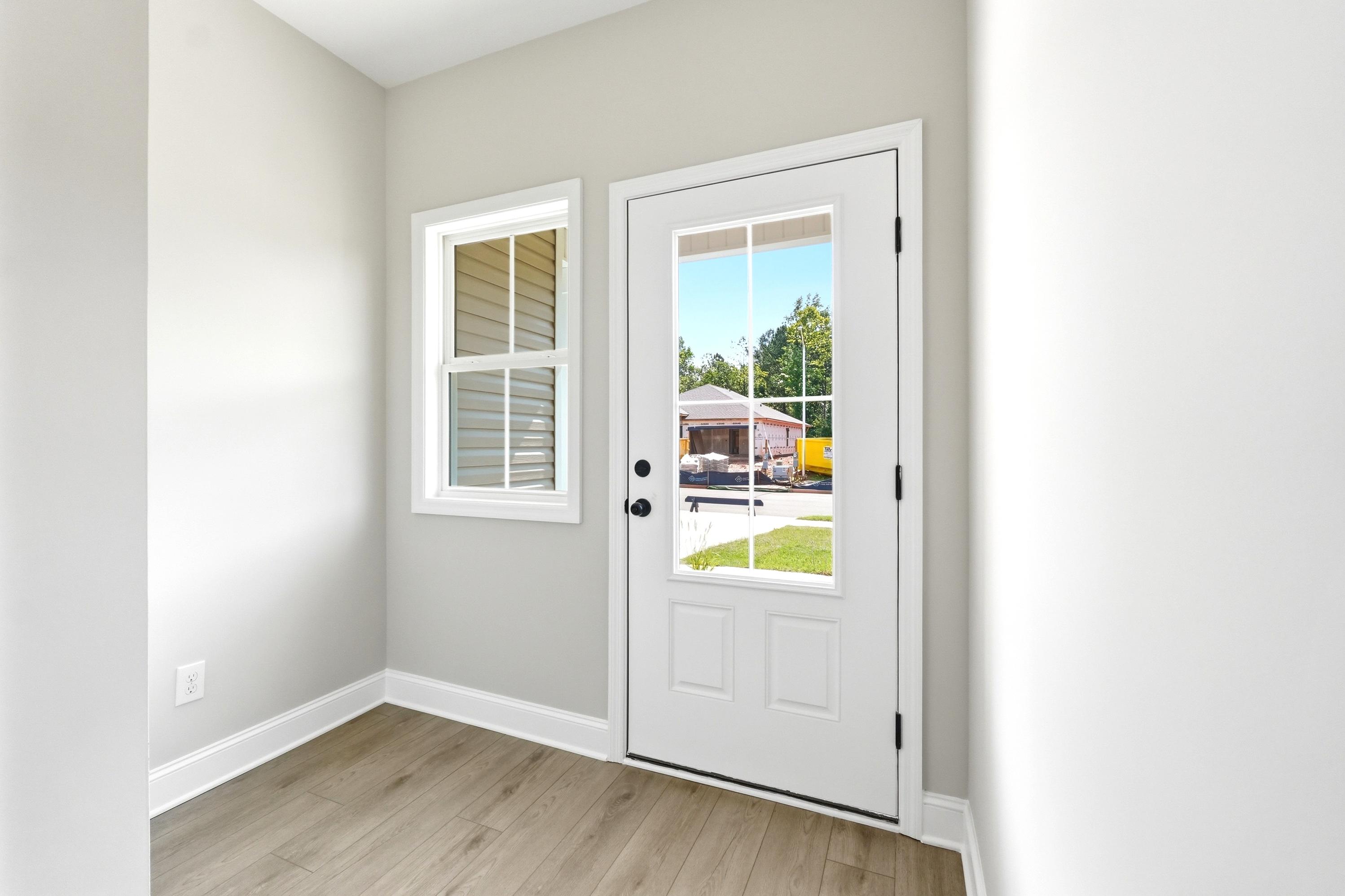 Bright entryway of The Russell A featuring modern light wood flooring, neutral walls, and a glass-paneled exterior door.