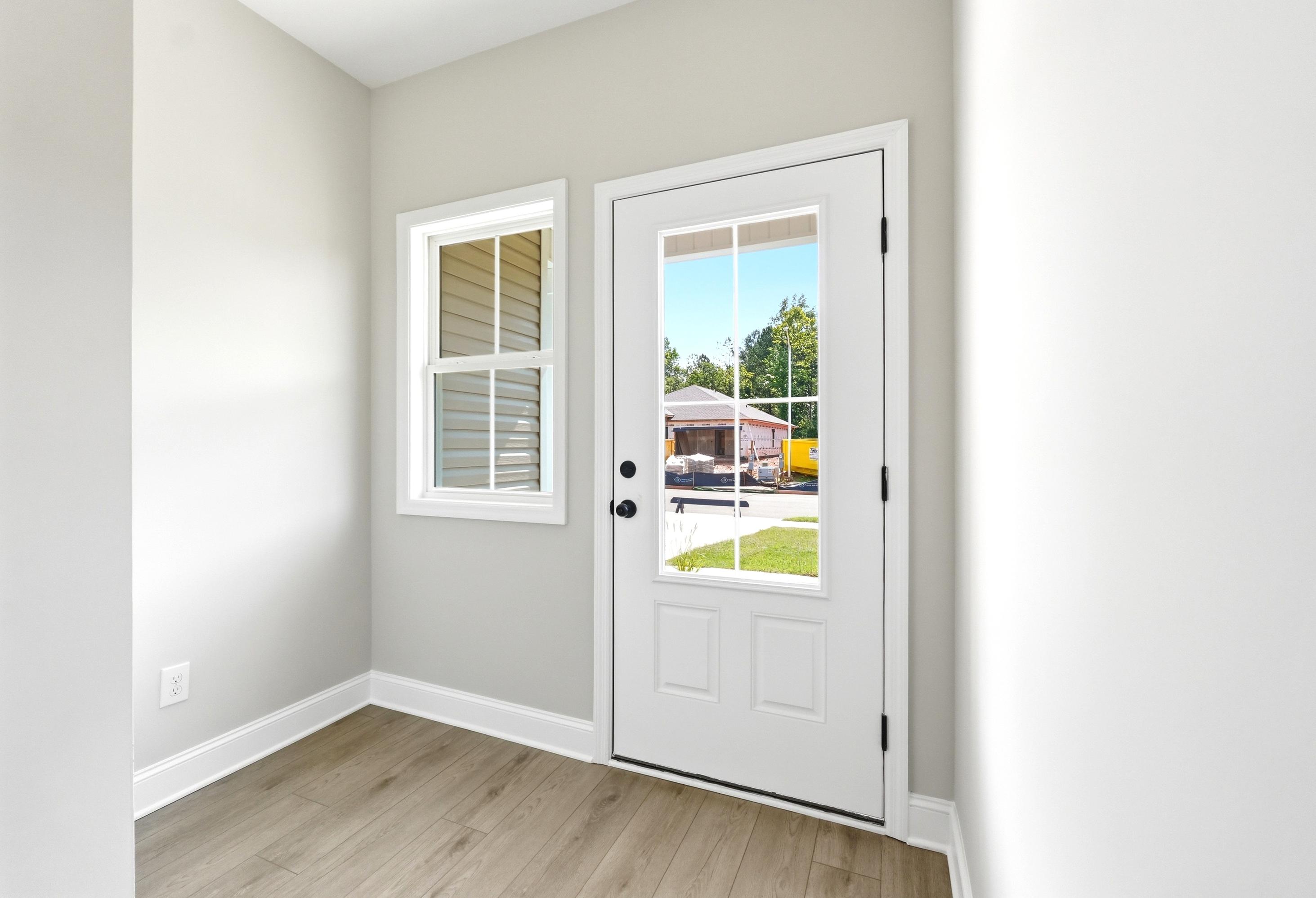 Bright entryway of The Russell A featuring modern light wood flooring, neutral walls, and a glass-paneled exterior door.