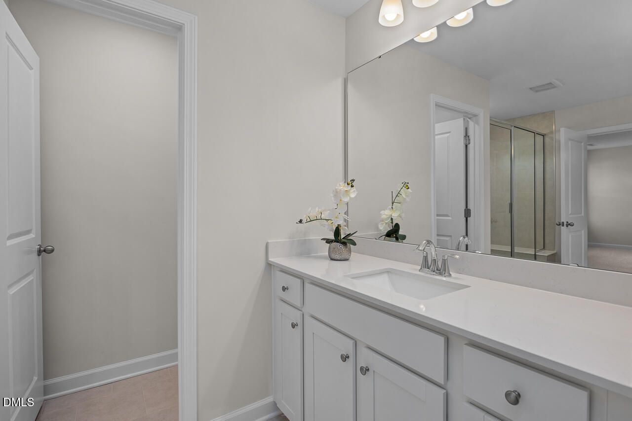 Elegant master bathroom with double white vanity, large mirror, potted orchid, and glass shower door in Davidson Homes Preston A, Lillington NC