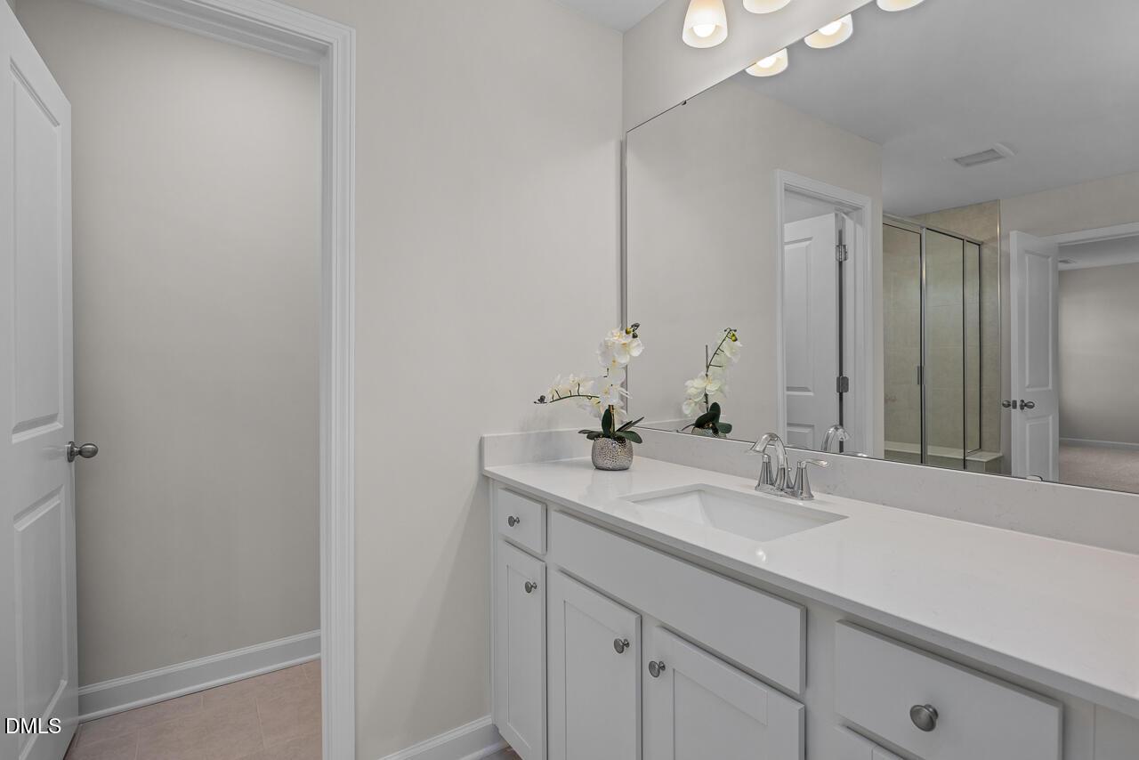 Elegant master bathroom with double white vanity, large mirror, potted orchid, and glass shower door in Davidson Homes Preston A, Lillington NC
