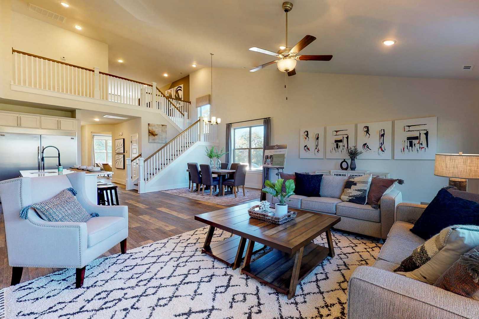 Spacious open-concept living room and kitchen in Liberty Creek home, Gallatin TN with hardwood floors, gray sofas, staircase, and ceiling fan