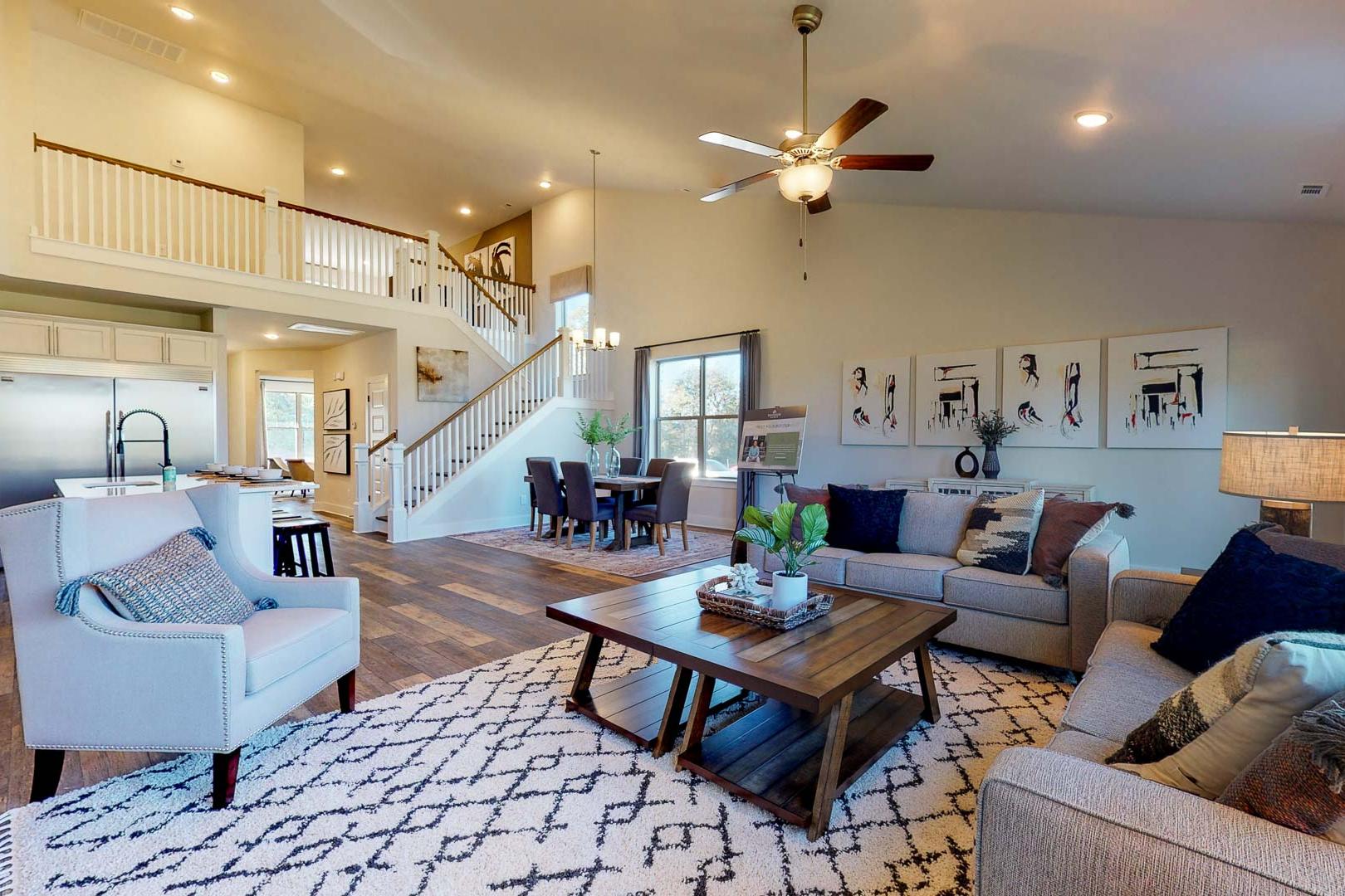 Spacious open-concept living room and kitchen in Liberty Creek home, Gallatin TN with hardwood floors, gray sofas, staircase, and ceiling fan