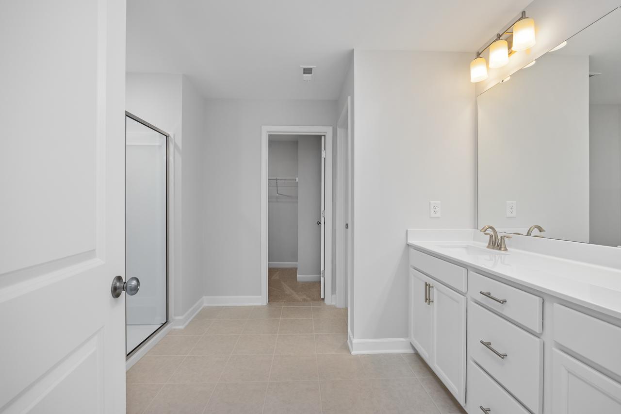 Spacious master bathroom in The Durham C featuring white double vanity, frameless glass shower, and neutral tile flooring