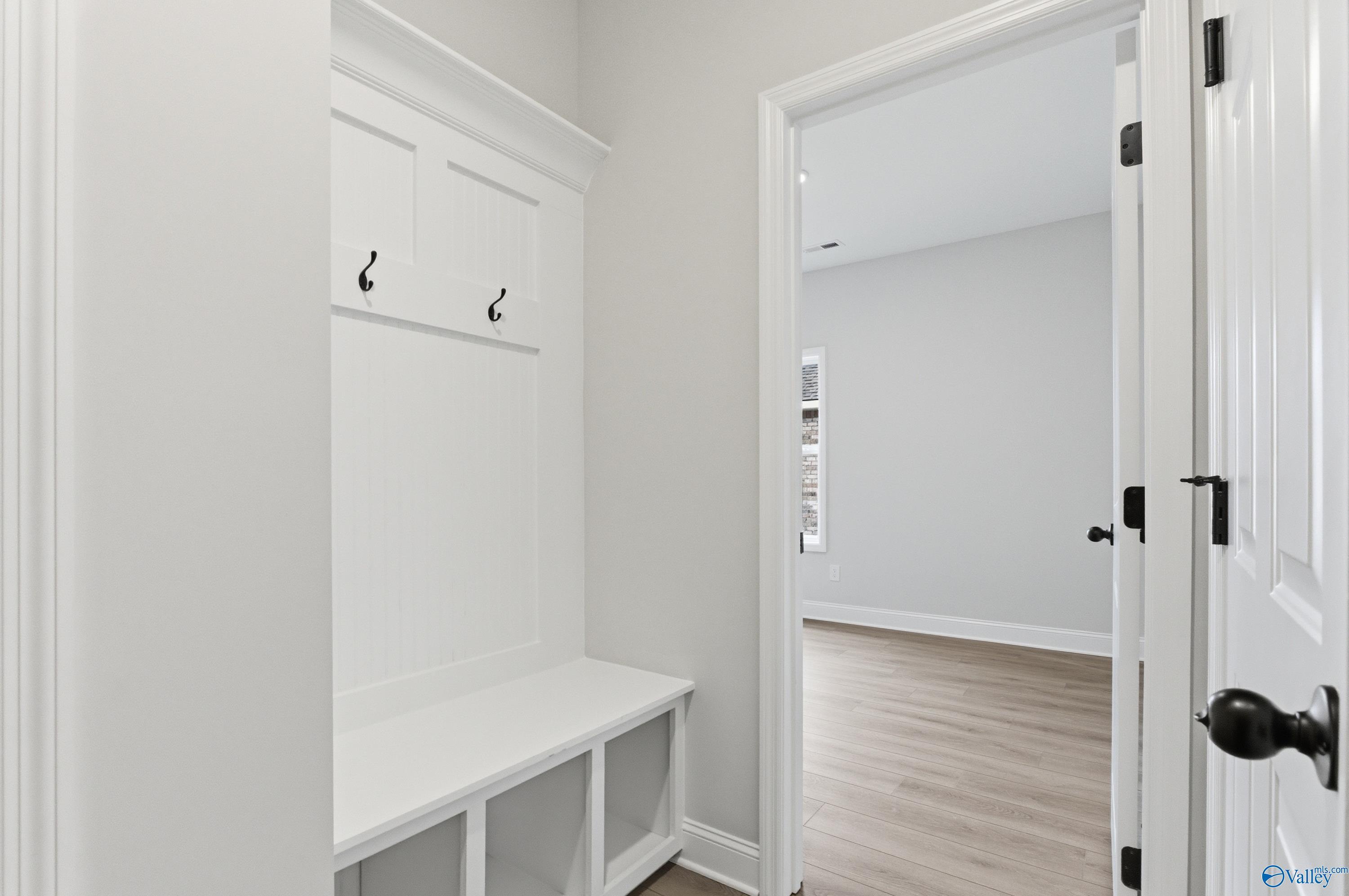 White built-in mudroom bench and coat hooks with open door in Davidson Homes The Daphne C, Huntsville, Alabama
