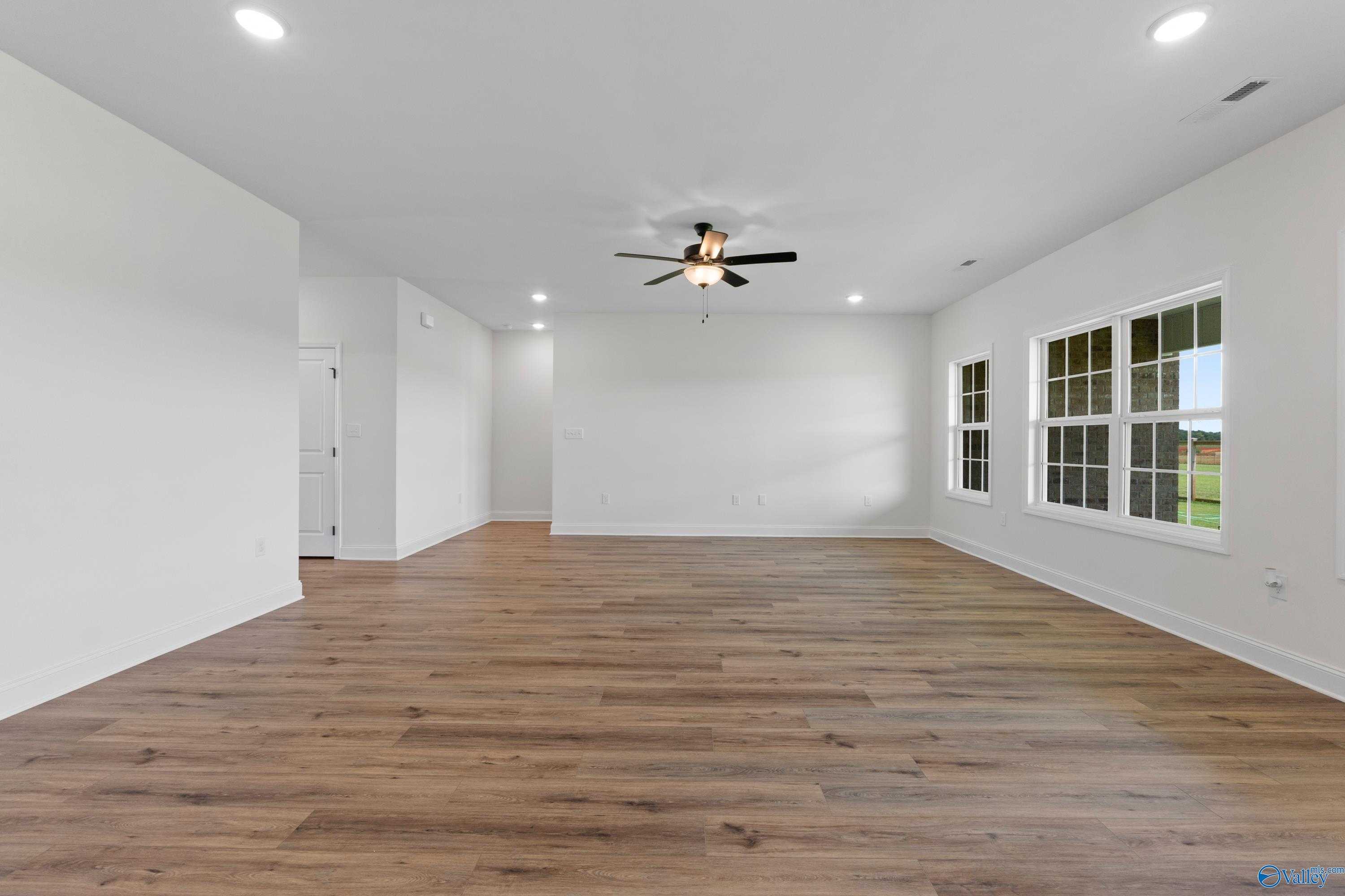 Spacious living room with hardwood floors, ceiling fan, and large windows in The Rockford B floor plan, Kendall Farms, Toney, Alabama
