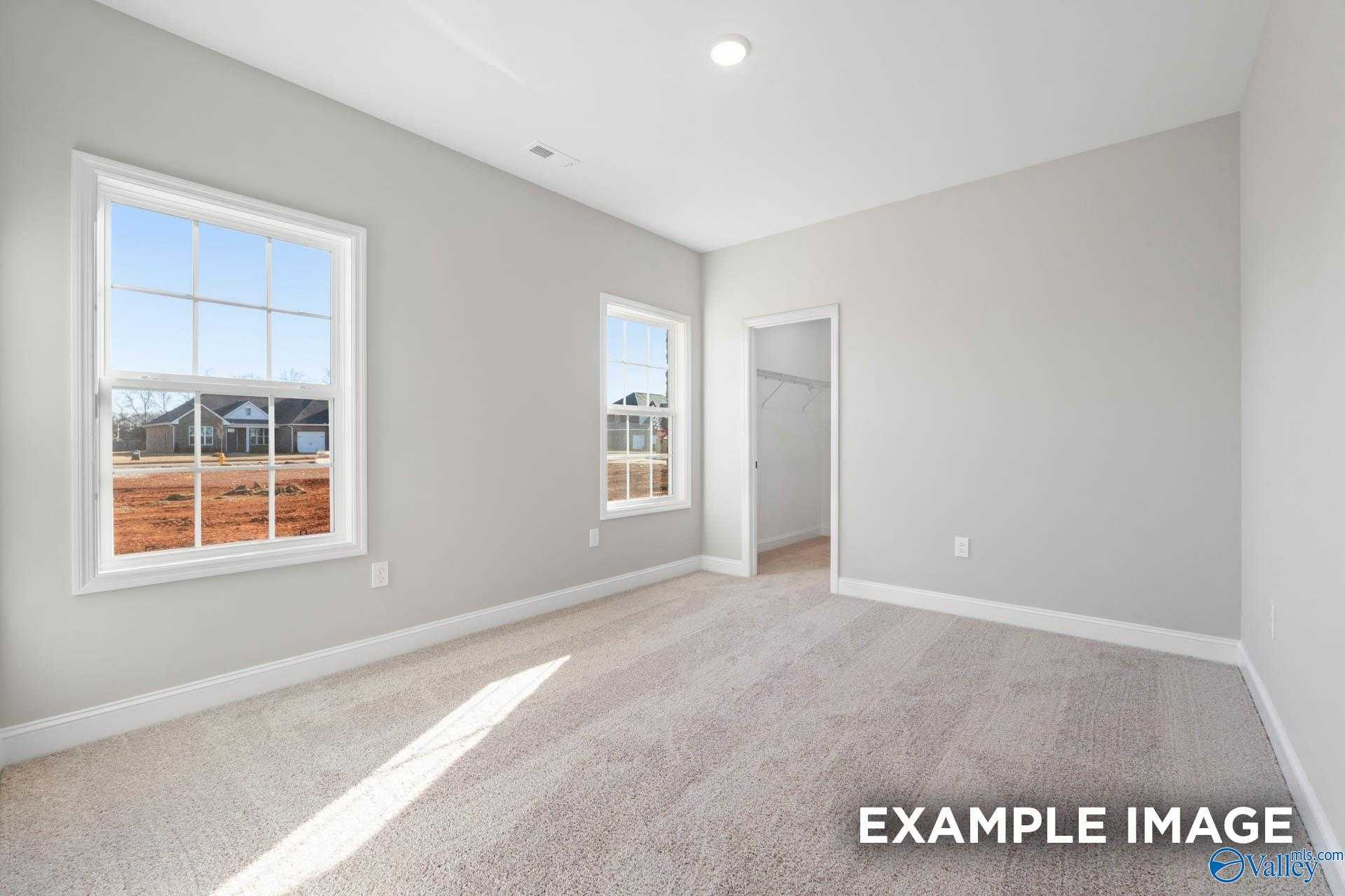 Sunny secondary bedroom with light gray walls, large sunny windows, and beige carpet in The Valencia home, Meridianville, Alabama