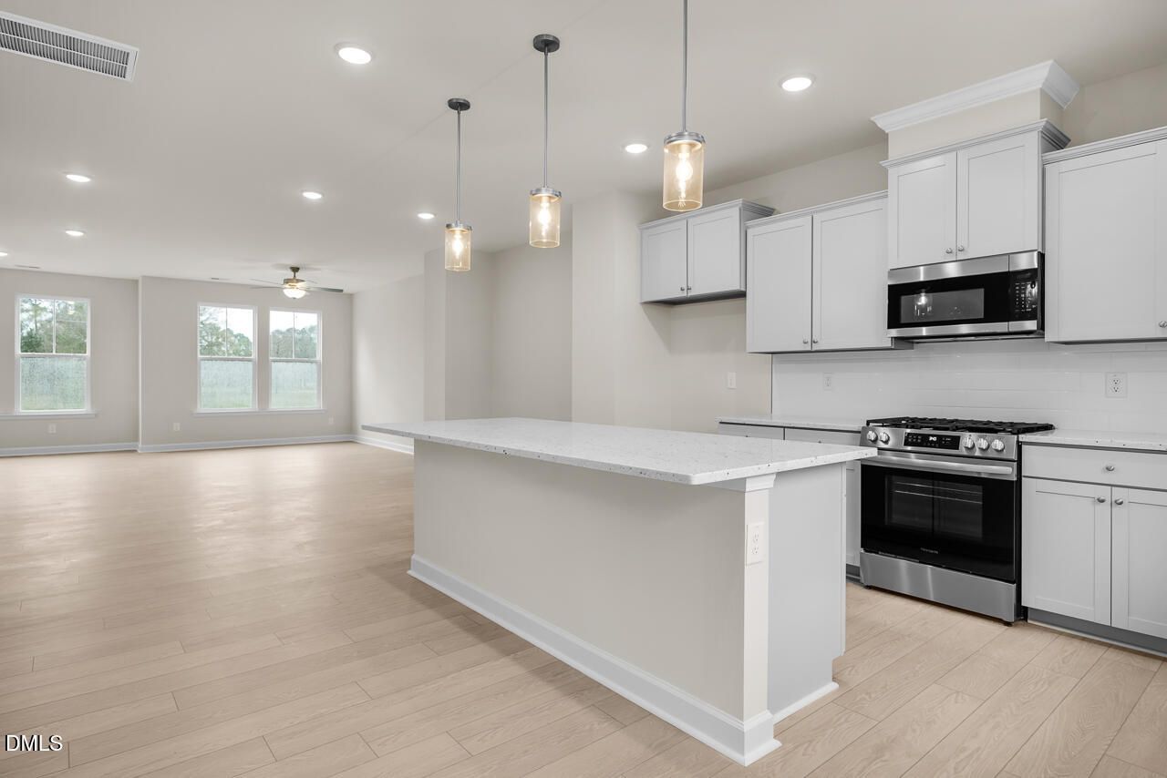 Modern kitchen with white shaker cabinets, speckled quartz island, stainless gas range, oven, and pendant lights in open living space, Knightdale NC