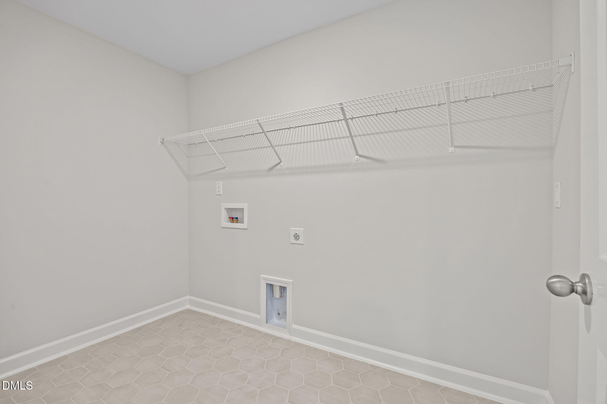 Spacious laundry room with white wire shelving, washer dryer hookups, and beige hexagonal tile floor in Davidson Homes The Willow D, Wendell, NC