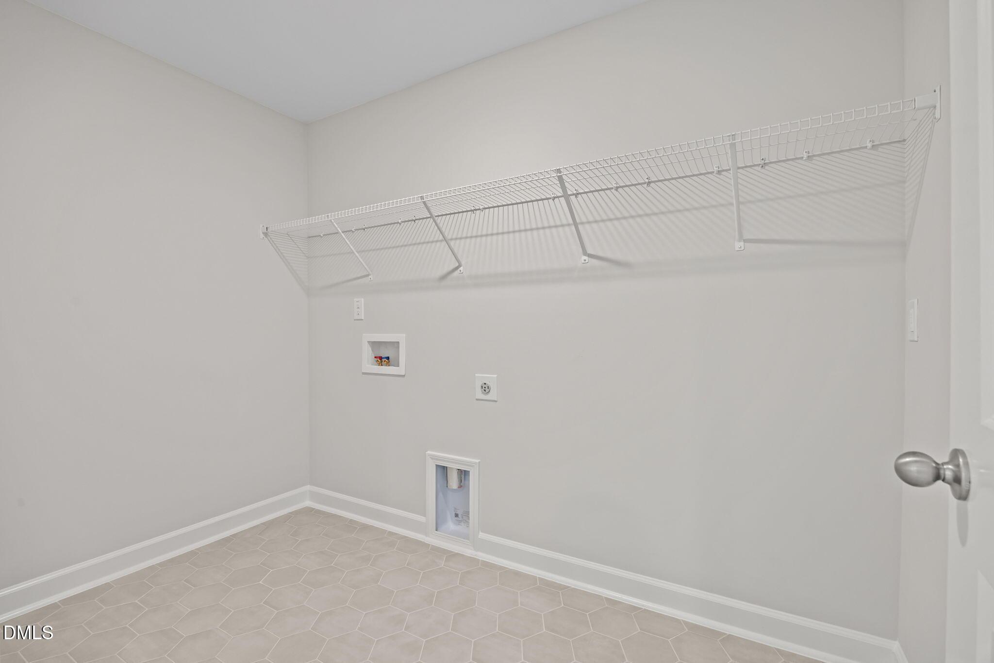 Spacious laundry room with white wire shelving, washer dryer hookups, and beige hexagonal tile floor in Davidson Homes The Willow D, Wendell, NC