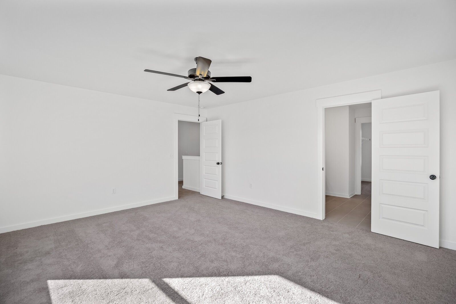 Spacious secondary bedroom with ceiling fan, gray carpet, and open bathroom door in Davidson Homes The Willow C, Gallatin, TN